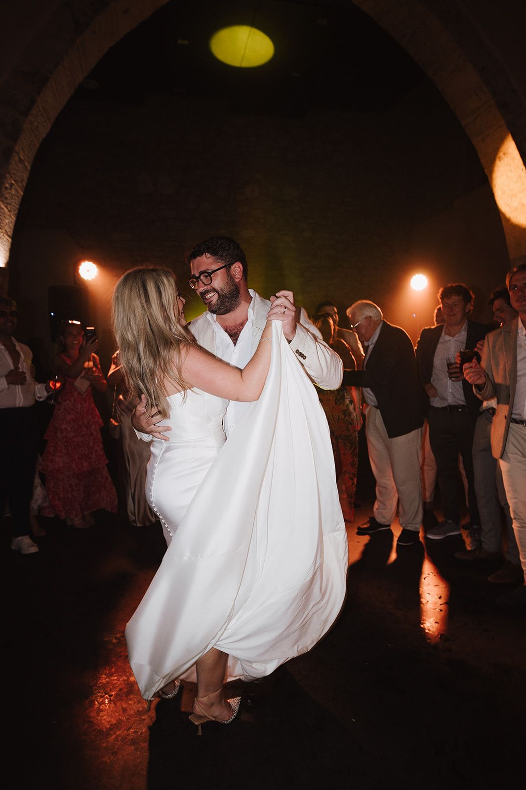 Bride and groom sharing first dance under stone arch with warm stage lighting and guests watching.