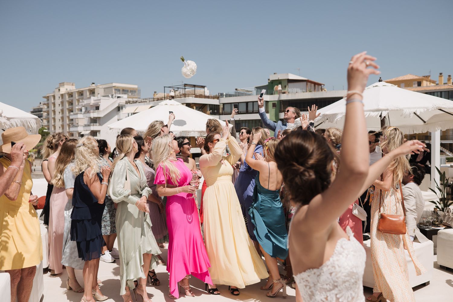 Wedding guests in colorful dresses dance and celebrate at outdoor reception.