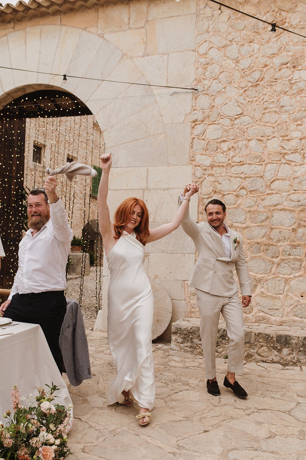 Bride in white halter gown and groom in beige suit make triumphant entrance at reception.