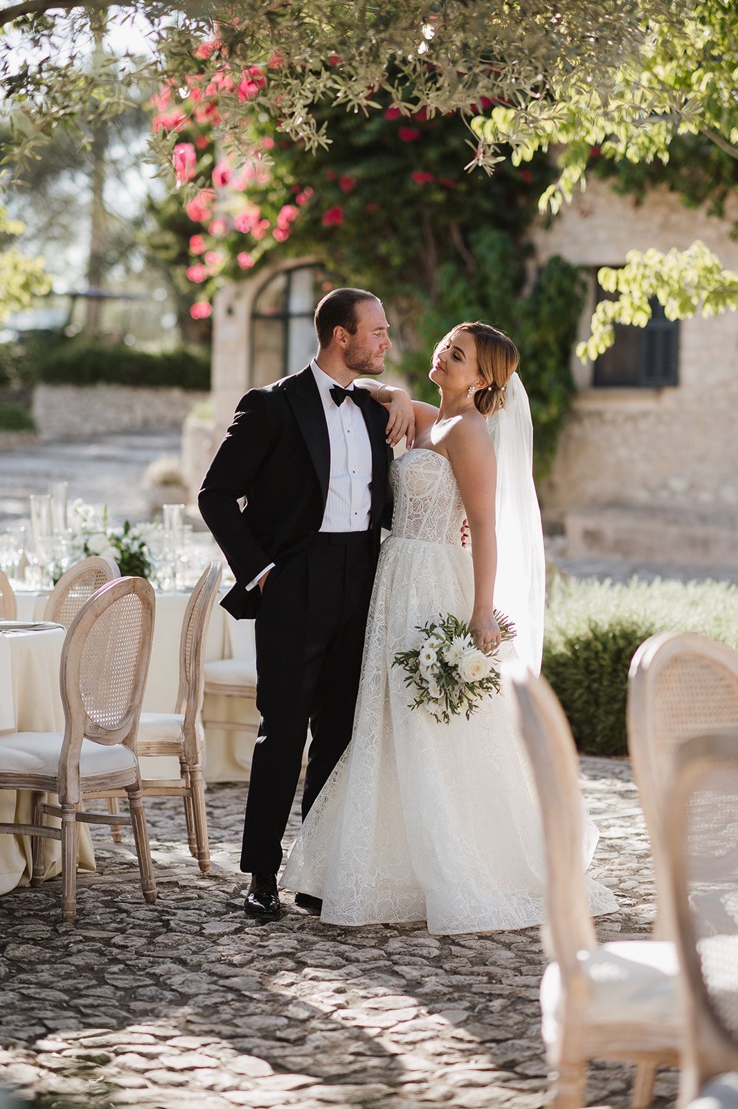 Bride and groom share romantic moment in courtyard under pink flowering trees.