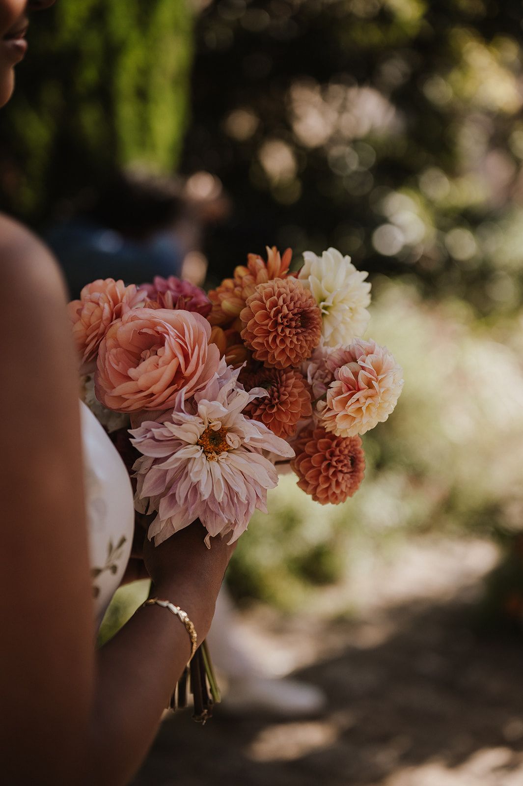 Close-up of bridesmaid holding lush bouquet of pink, coral, and cream dahlias and roses.