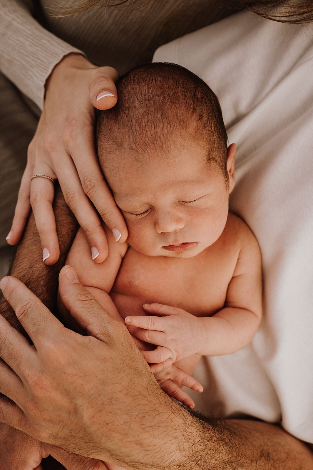 Peaceful newborn baby sleeping in parents arms during newborn photo session.