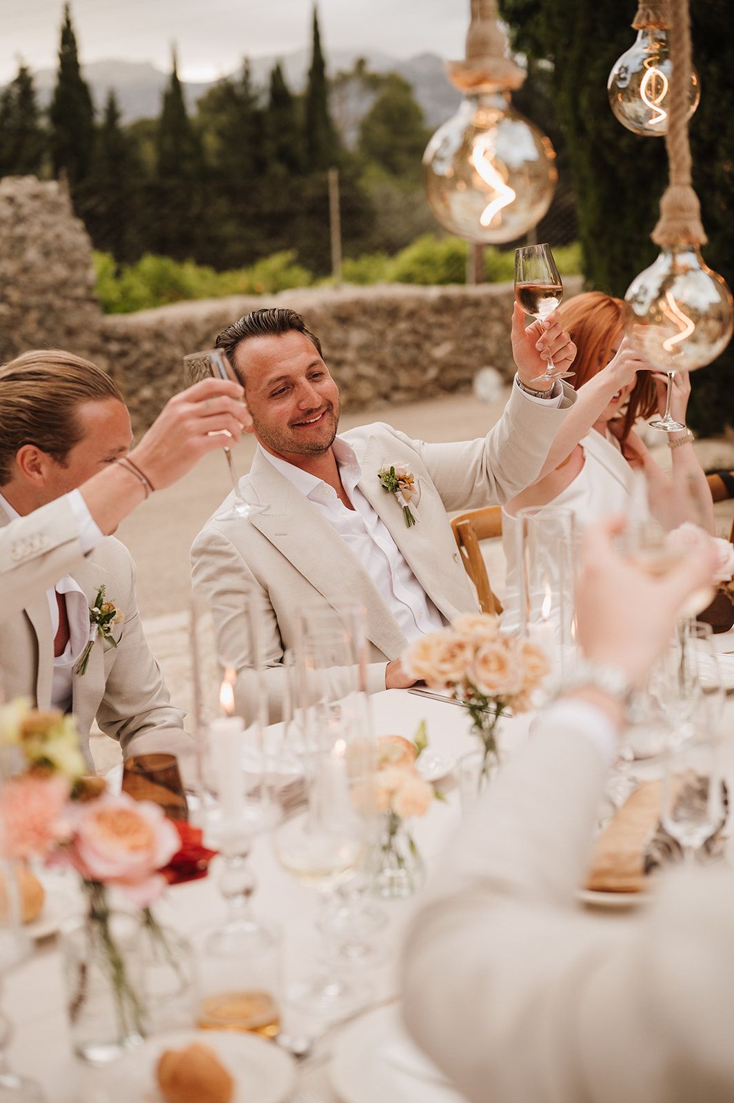 Wedding guests raising champagne glasses in a toast at an outdoor reception dinner.
