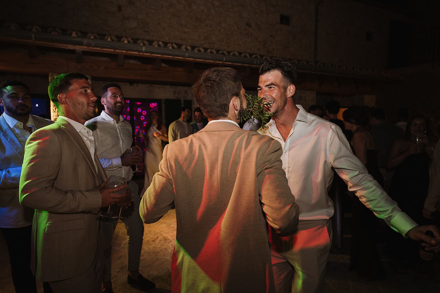 Groom greeting guests with handshake on colorful lit dance floor at outdoor evening wedding party.