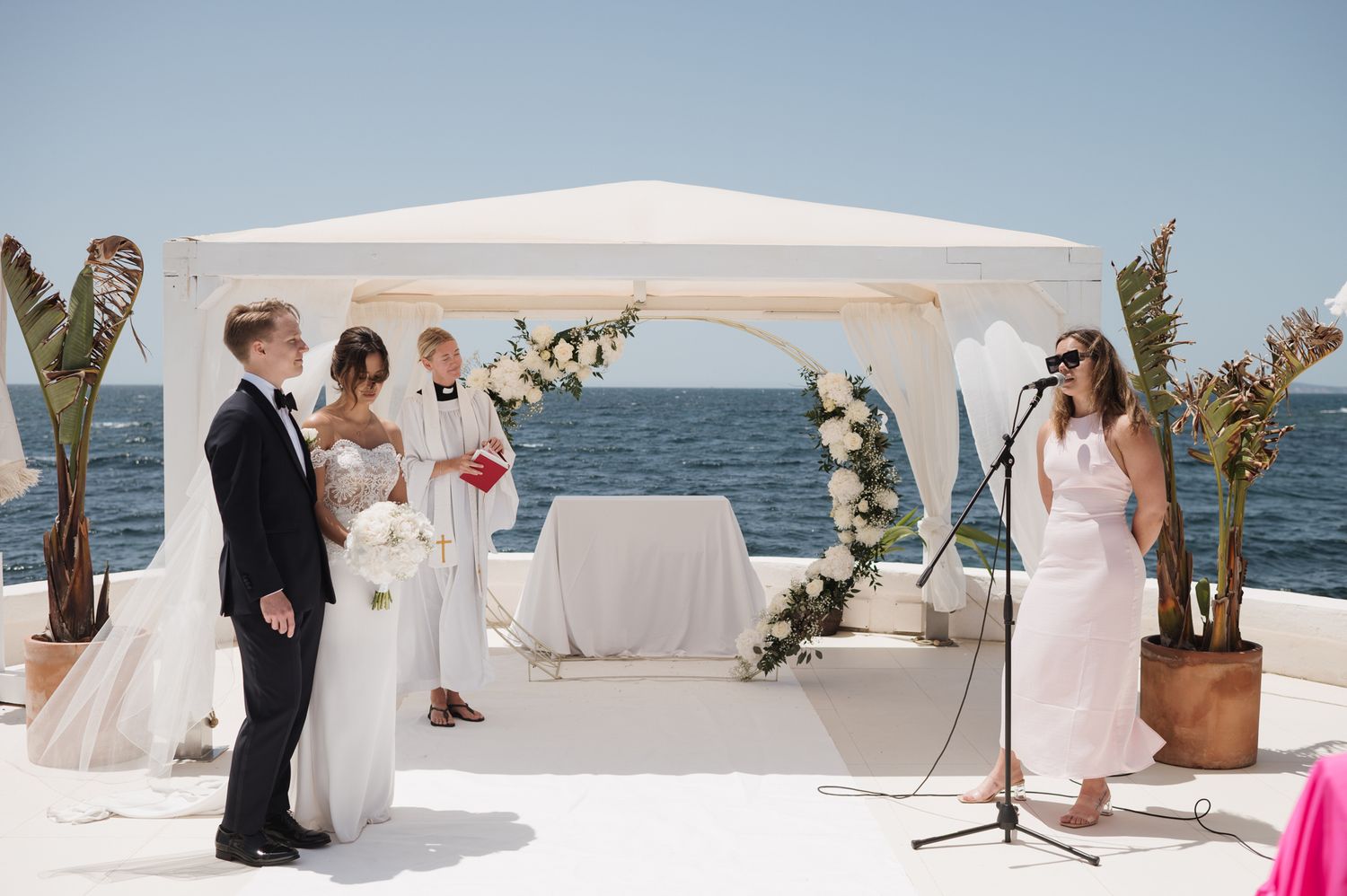 Outdoor seaside wedding ceremony under white canopy with ocean backdrop.