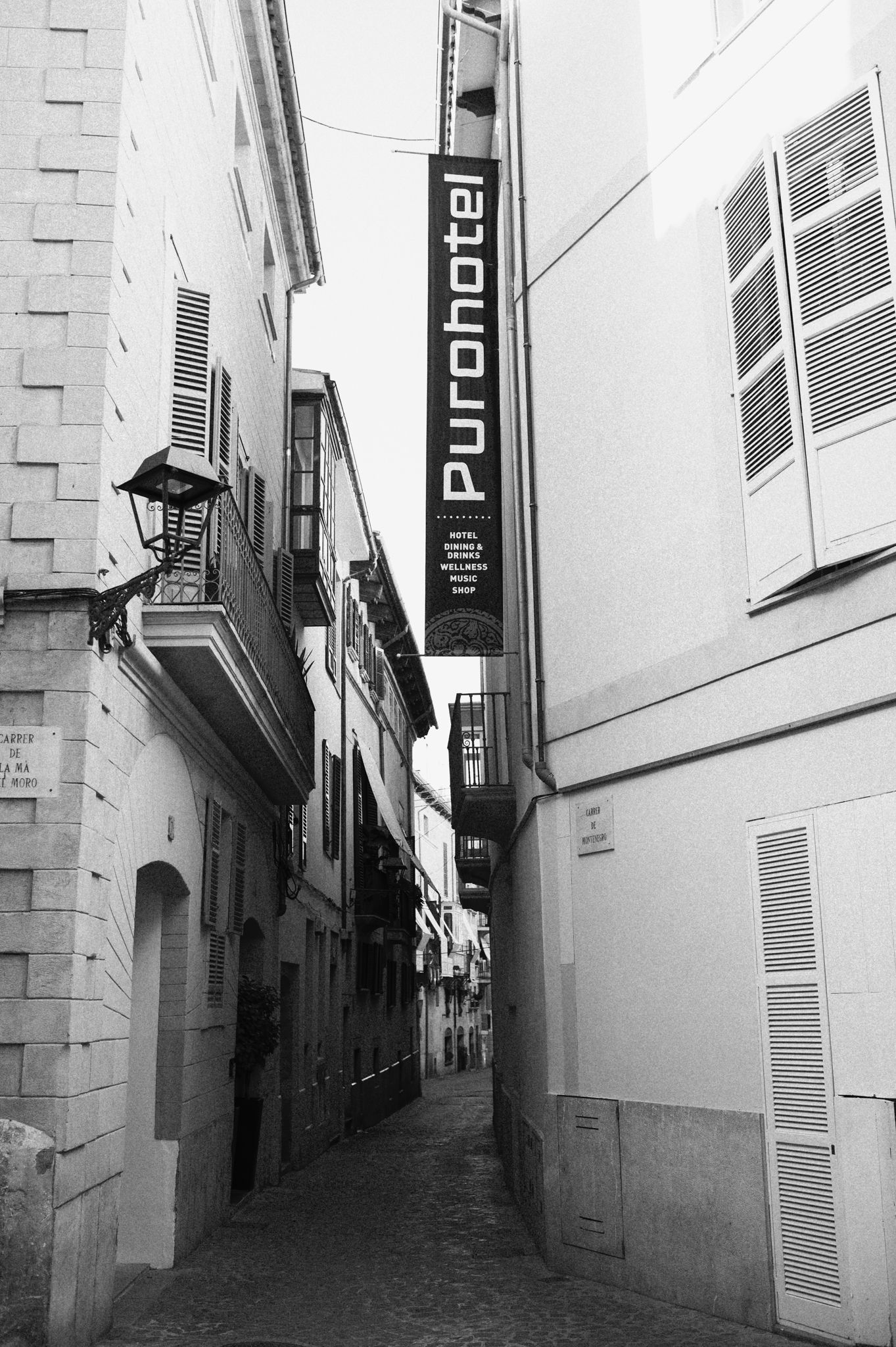 Black and white photo of a narrow European alley with a Puro Hotel sign on a building facade.