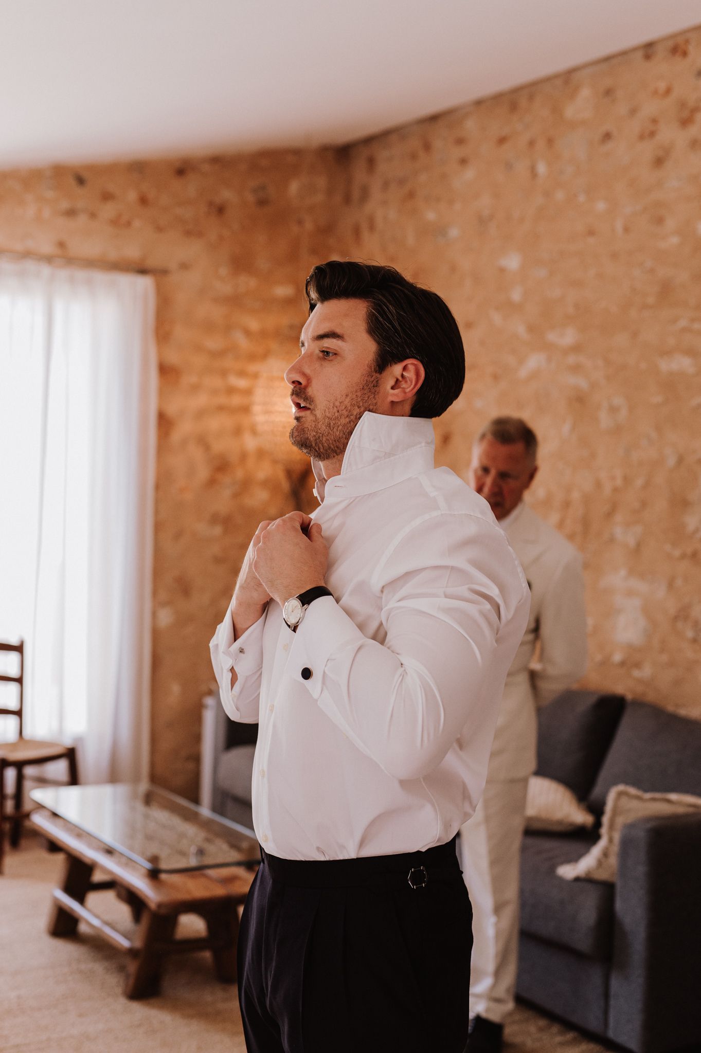 Groom adjusting his white dress shirt collar while getting ready for his wedding ceremony.
