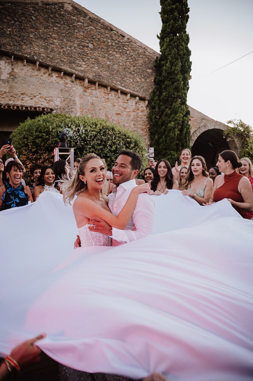 Joyful bride and groom celebrate surrounded by cheering guests during outdoor wedding reception toss.
