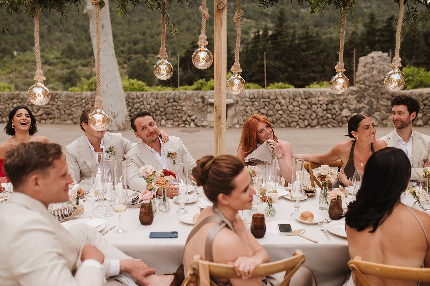 Wedding guests laughing and enjoying conversation at a decorated outdoor reception dinner table.