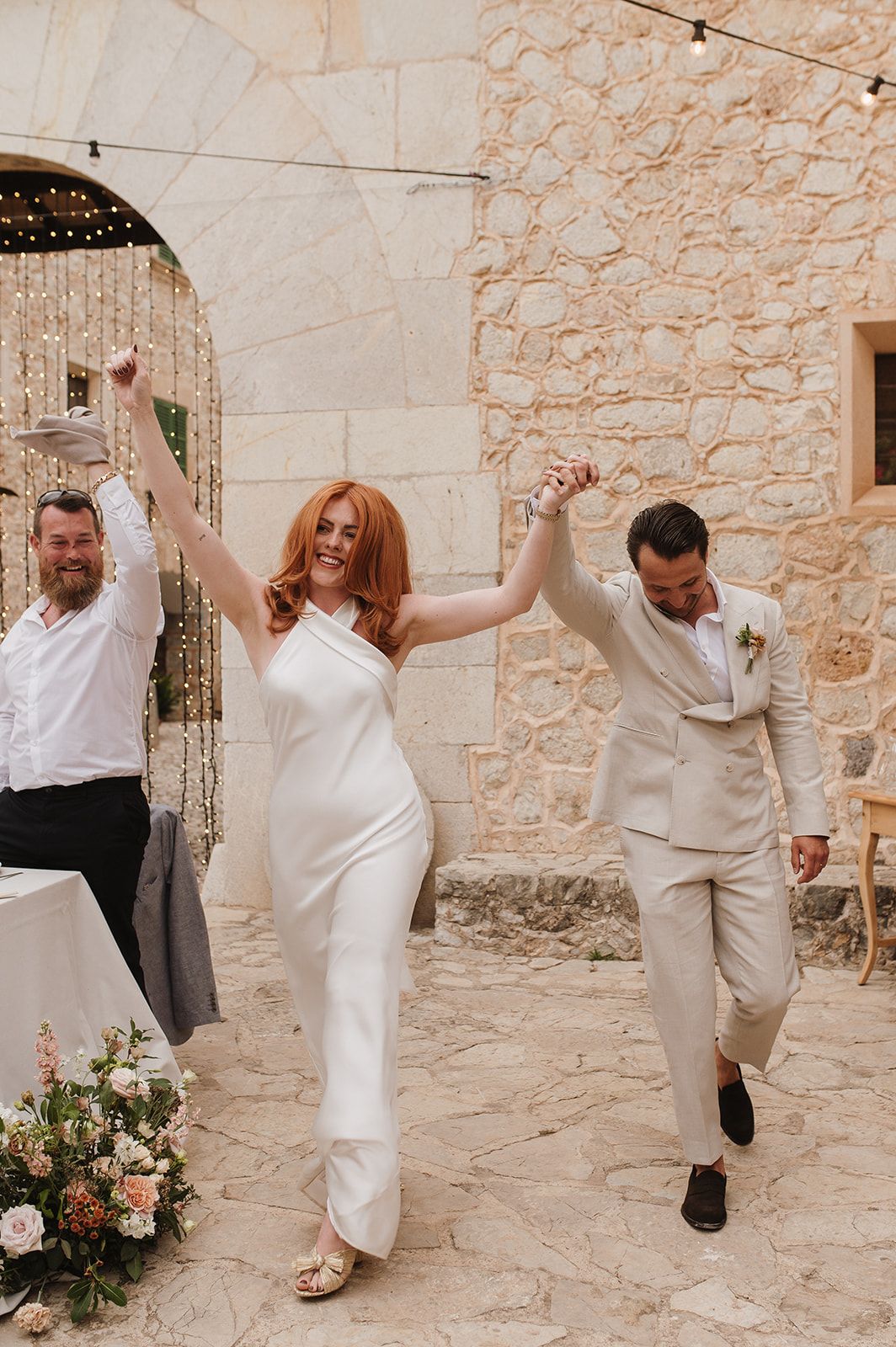 Radiant bride in white halter dress and groom in beige suit celebrate their grand reception entrance.