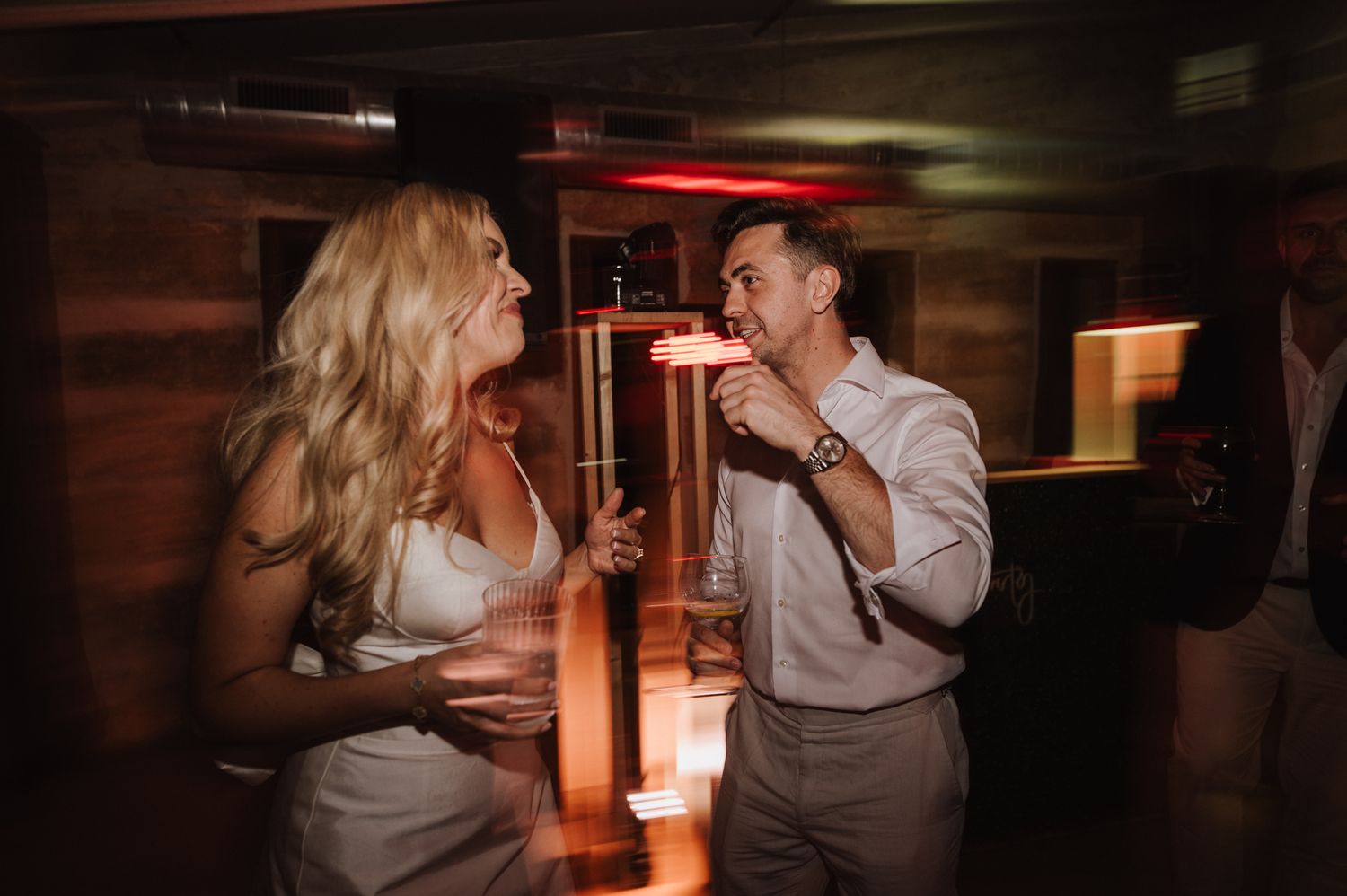 Bride and groom laughing and dancing together at dimly lit wedding reception party.