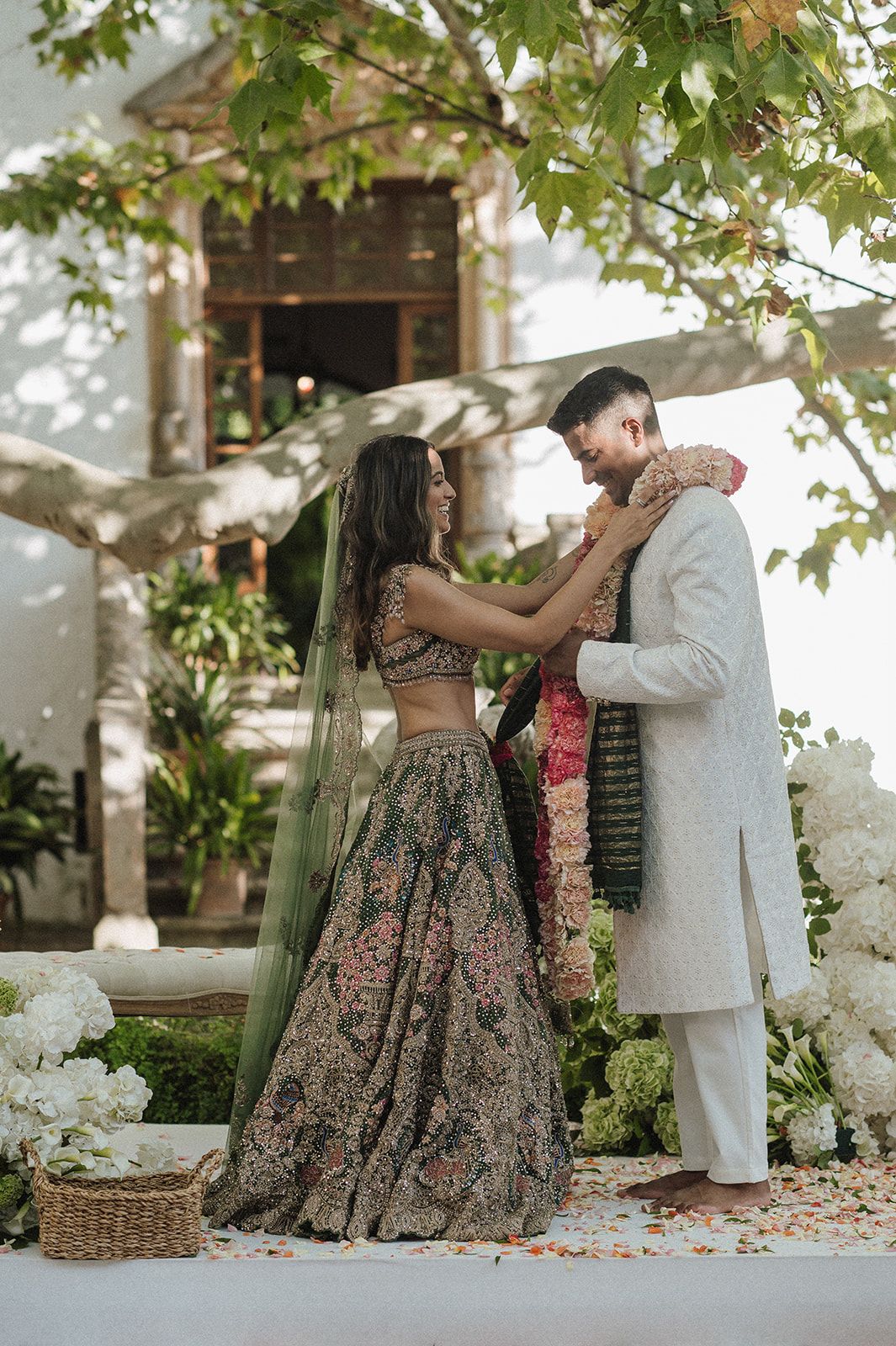 Bride placing floral garland on groom during Indian wedding ceremony with white flower decor.