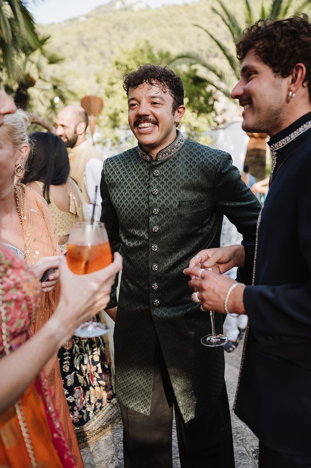 Man in green embroidered sherwani smiling and socializing at an Indian wedding reception.