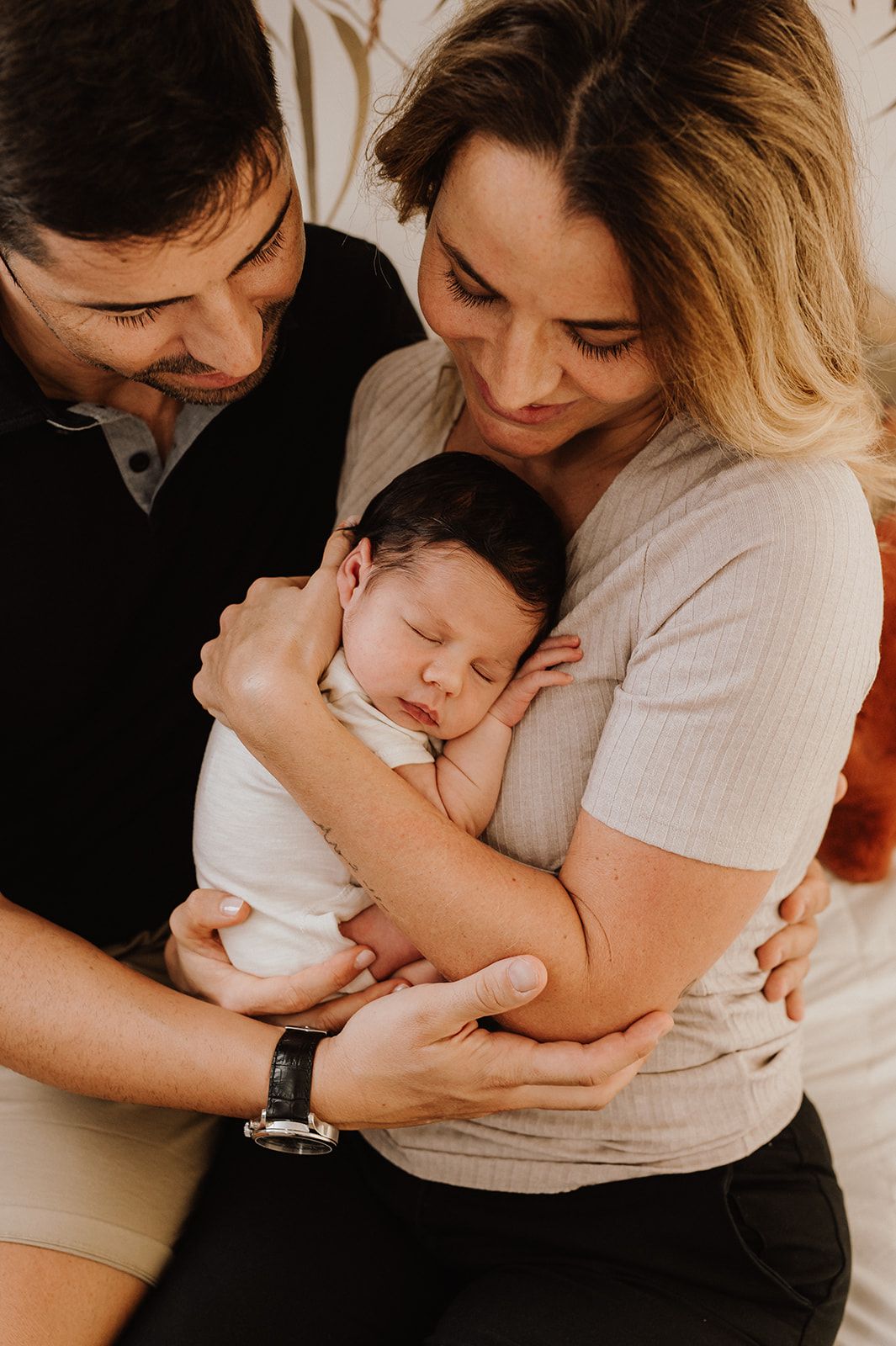 New parents lovingly cradle their sleeping newborn baby together, sharing a tender family moment.