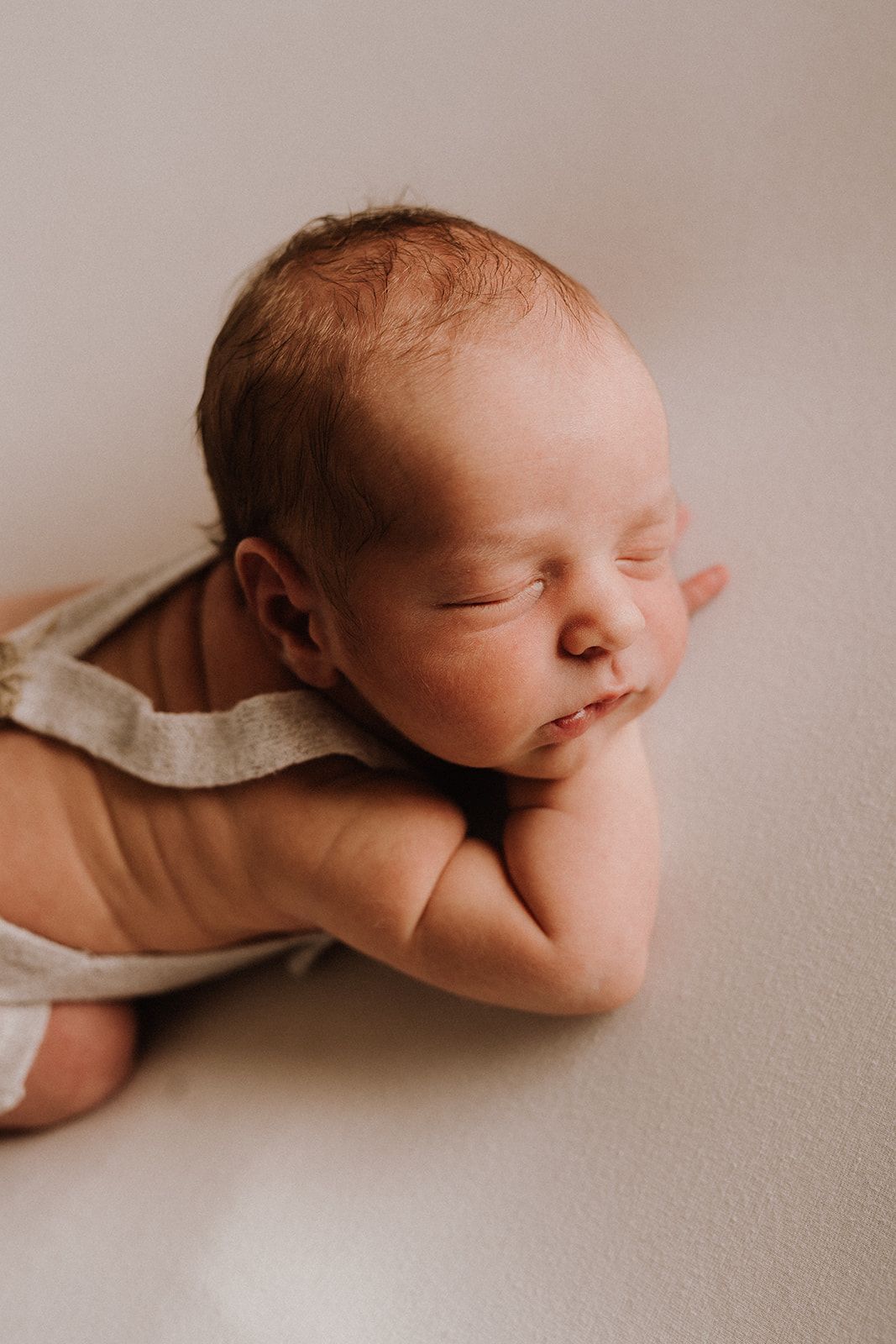 Peaceful newborn baby sleeping on white surface, wearing a neutral onesie, with hands tucked under chin.