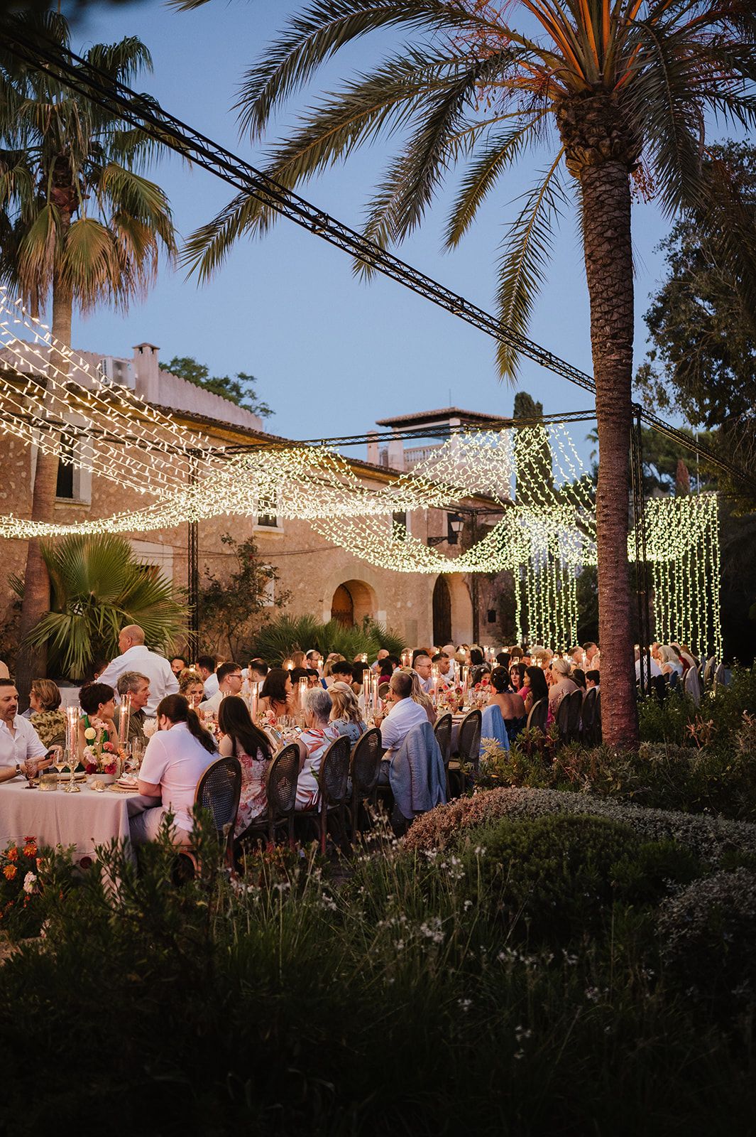 Guests dine under fairy lights at magical outdoor evening reception.