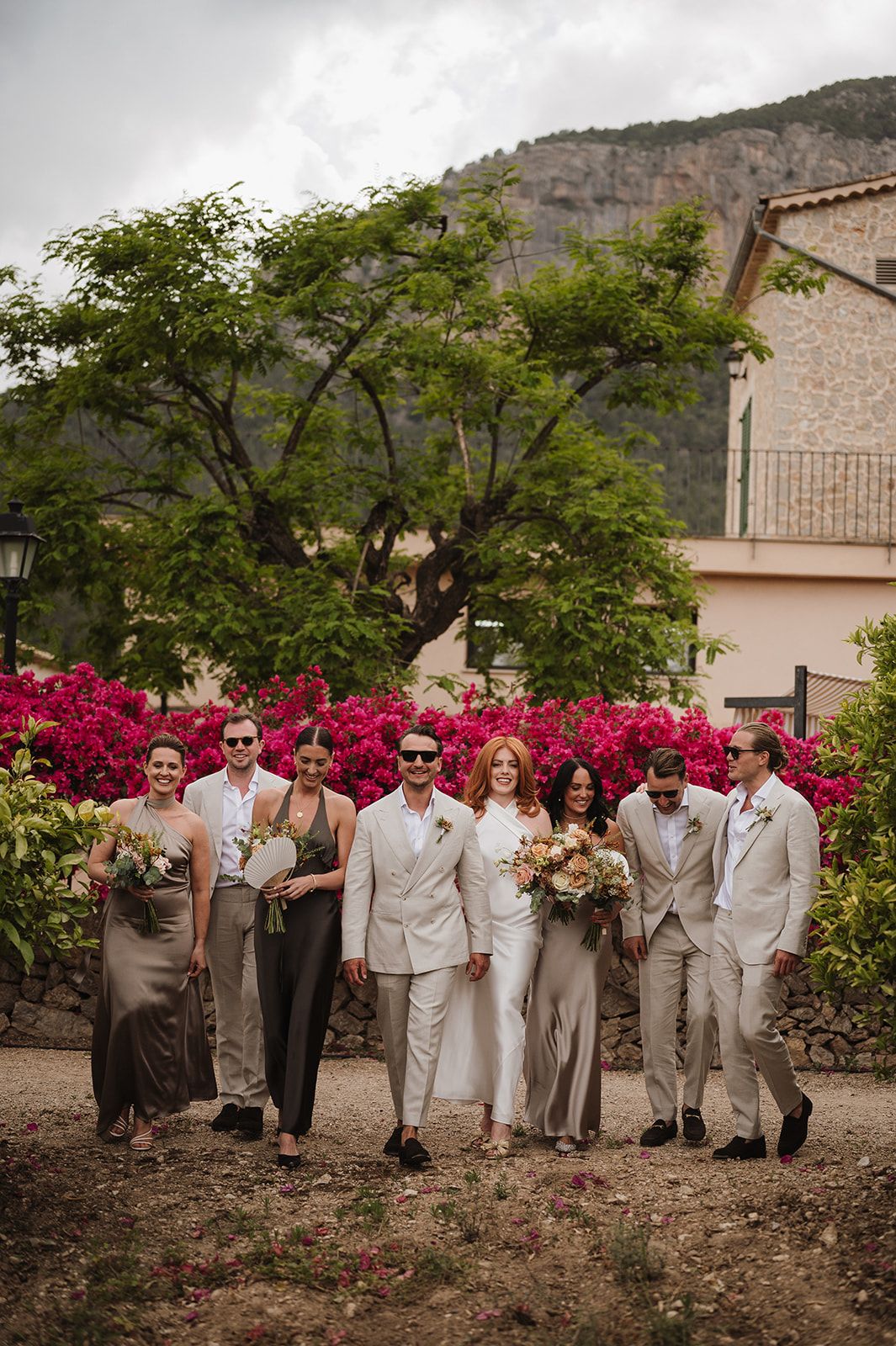 Wedding party poses before vibrant pink bougainvillea with mountain views at outdoor venue.