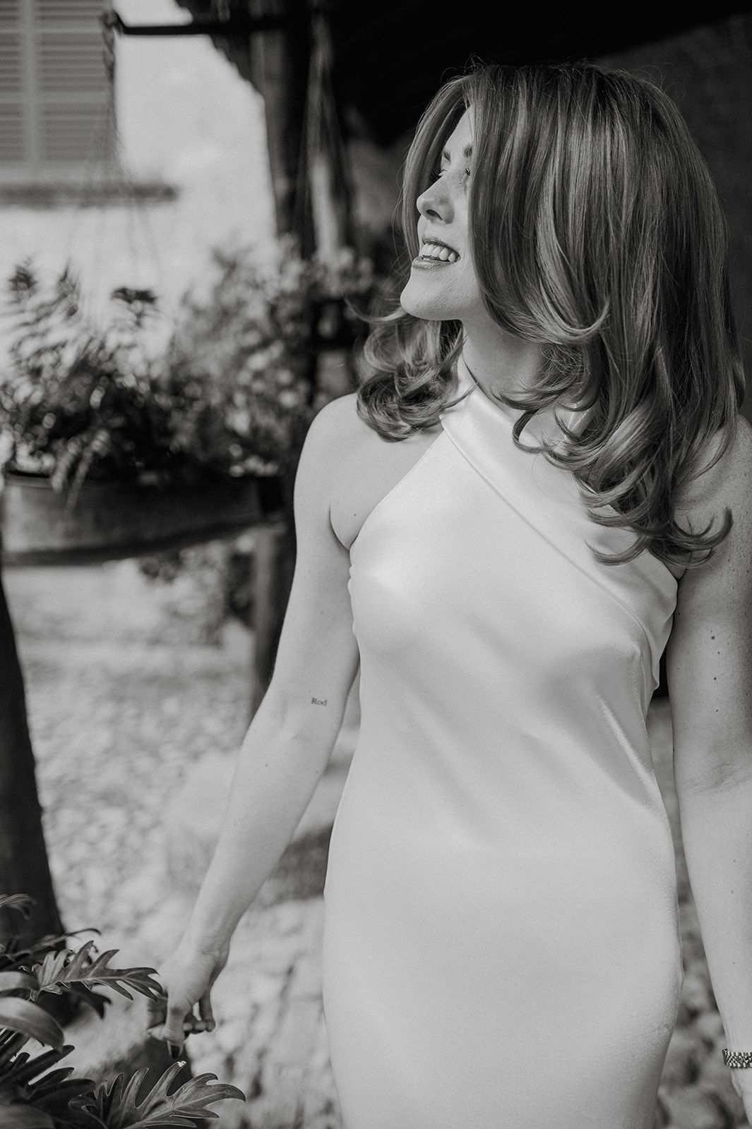 Black and white portrait of a smiling bride in a halter neck wedding dress outdoors.