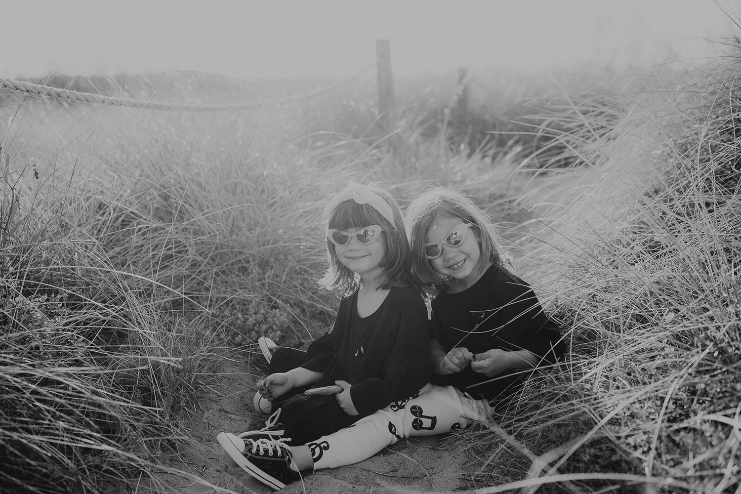 Two young sisters sitting together in tall grass in a black and white photo.