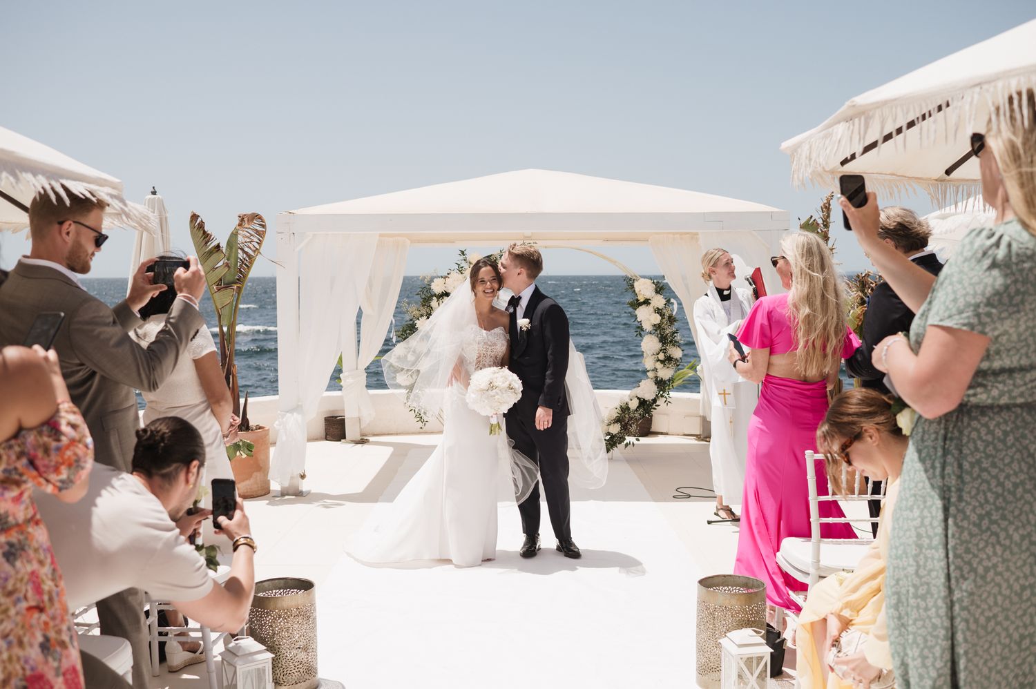 Bride and groom sharing their first kiss at an outdoor oceanfront wedding ceremony.
