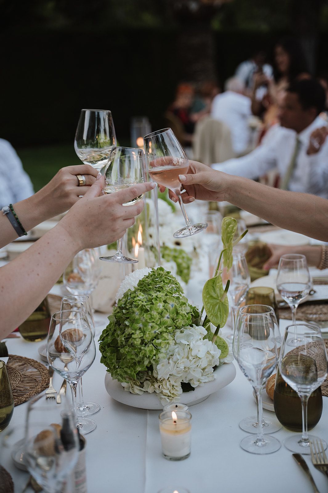 Guests clinking wine glasses in a toast over floral centerpiece at outdoor wedding reception.