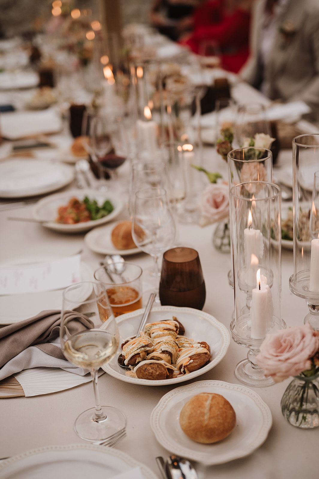 Elegant wedding reception table set with candles, pink roses, wine glasses, and artisan bread rolls.