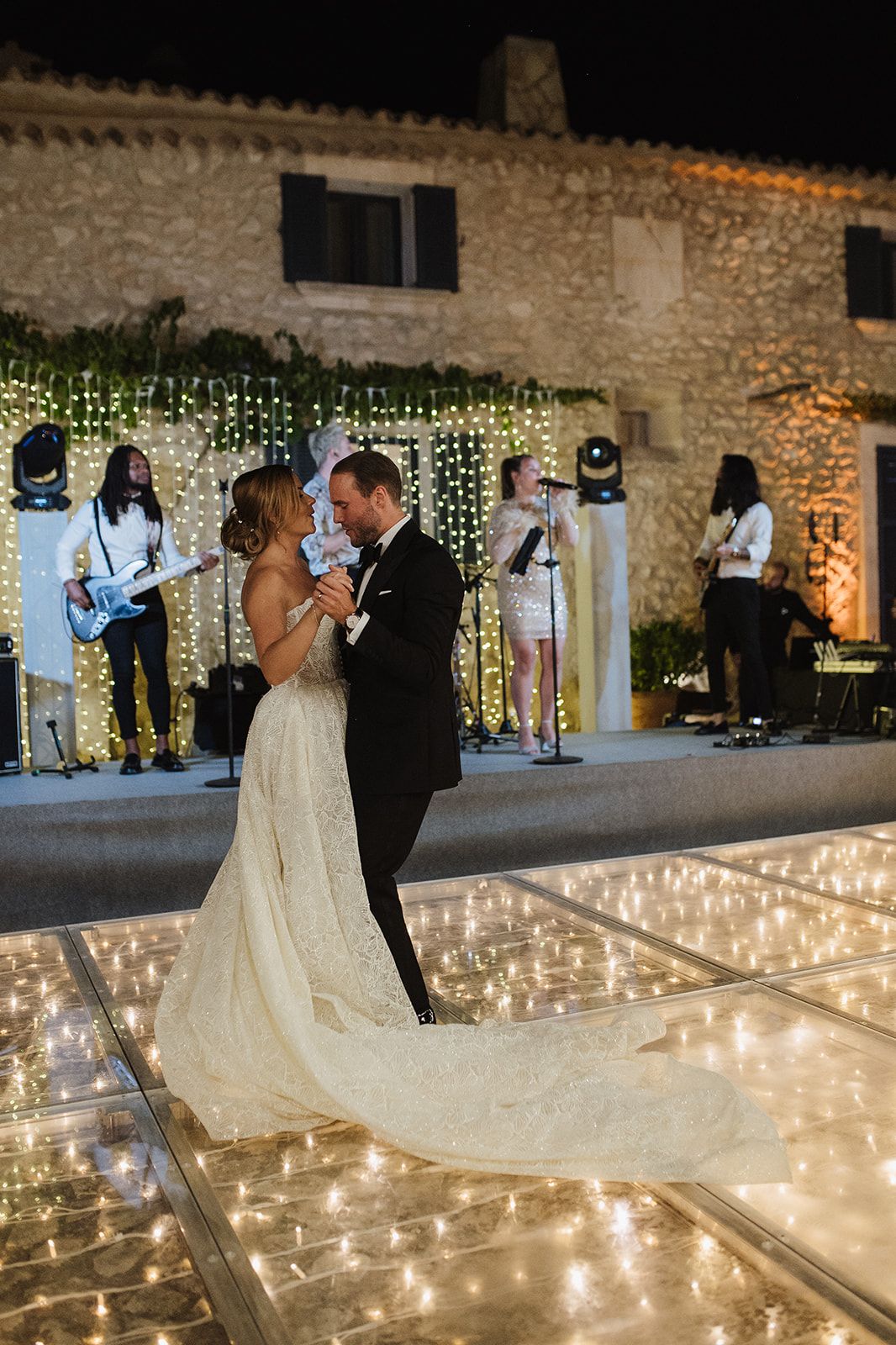 Bride and groom share first dance on illuminated floor with live band performing at night wedding.