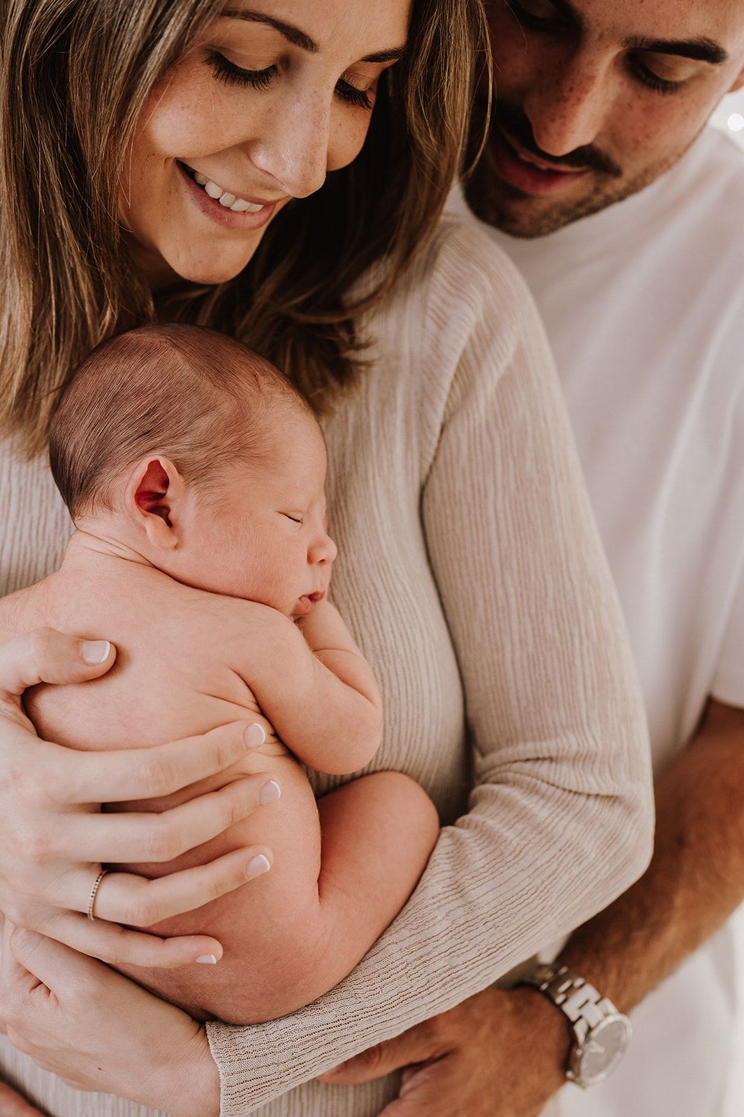 Smiling parents tenderly cradling their sleeping newborn baby, captured in a warm, intimate family portrait.