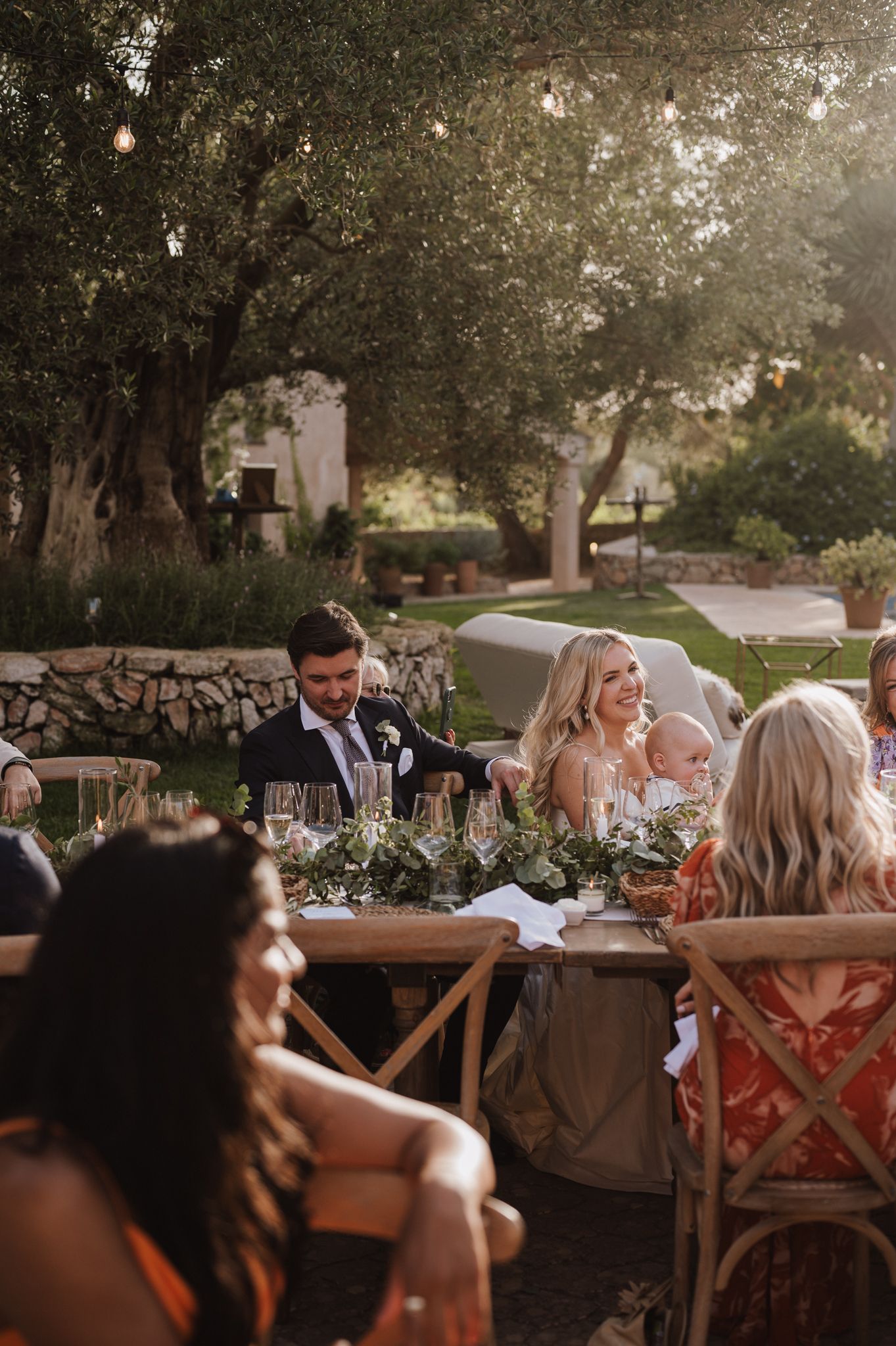 Bride and groom laughing together at their outdoor wedding reception dinner table at sunset.