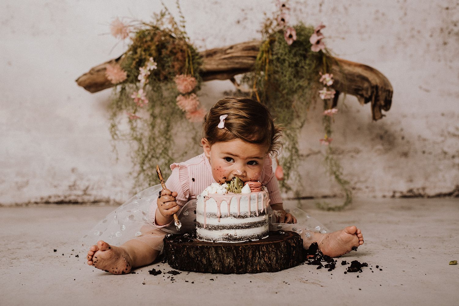 Baby girl smashing a white cake on a wooden slab during a first birthday cake smash photo session.