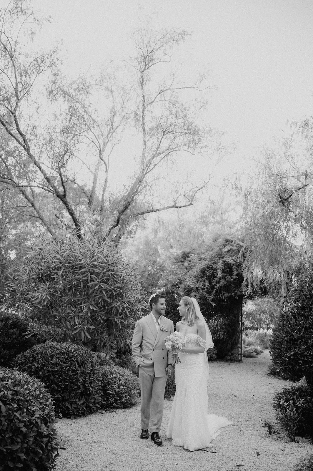 Black and white portrait of bride and groom standing together in a lush garden pathway after wedding.