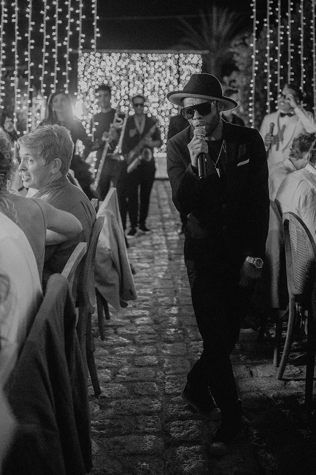 Wedding entertainer singing into microphone while walking through candlelit outdoor reception aisle.