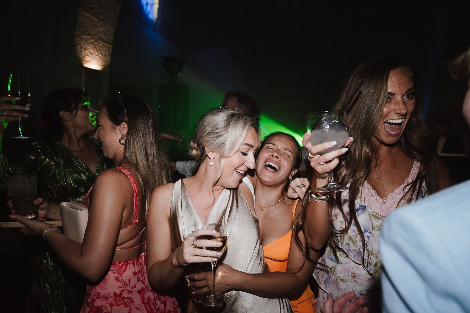 Group of women laughing and dancing together at a lively wedding reception party.