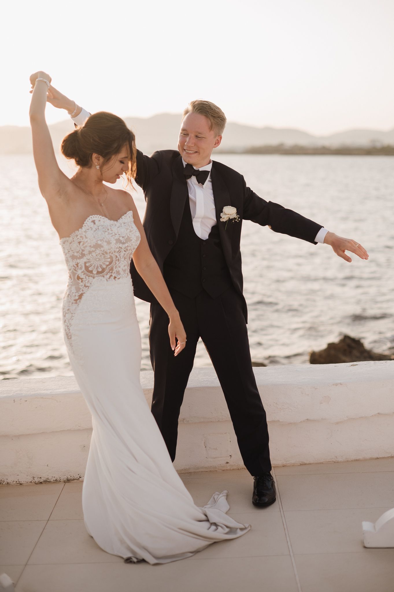 Groom spinning bride in lace mermaid wedding dress during sunset portrait by the ocean.