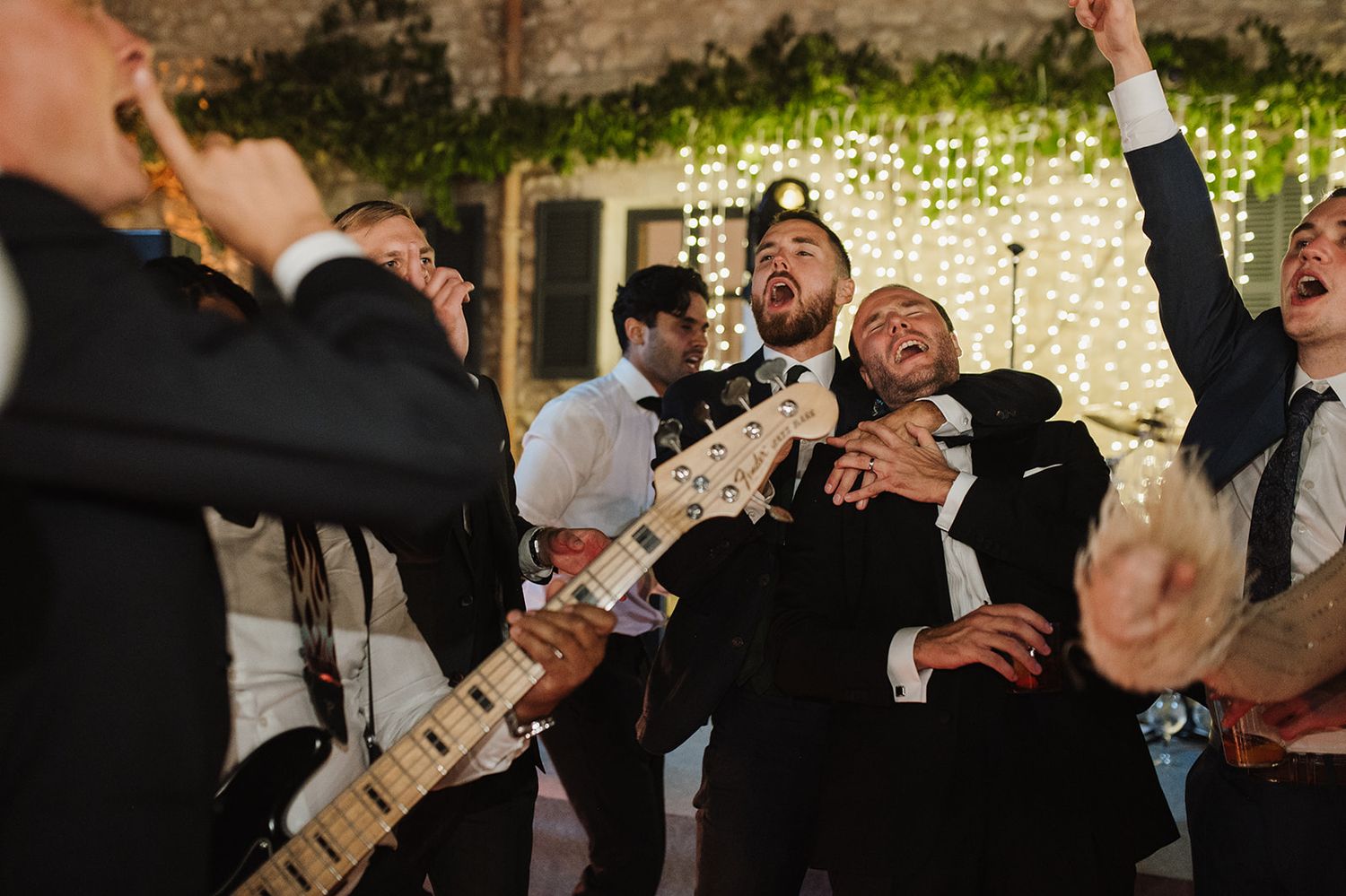 Excited wedding guests sing along with live band guitarist at a lively outdoor evening reception.