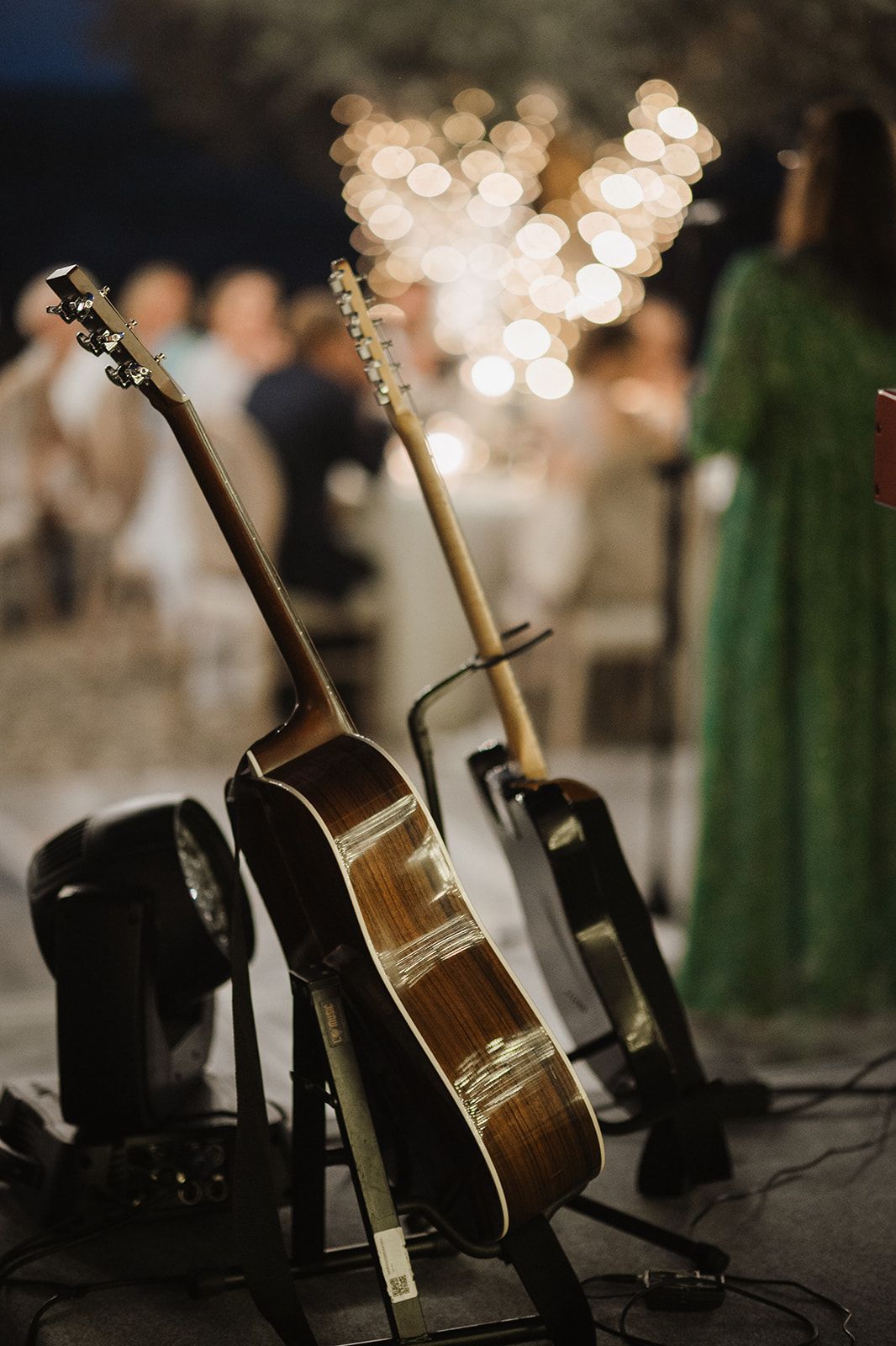 Acoustic guitars on stands at an outdoor wedding reception with bokeh string lights in background.