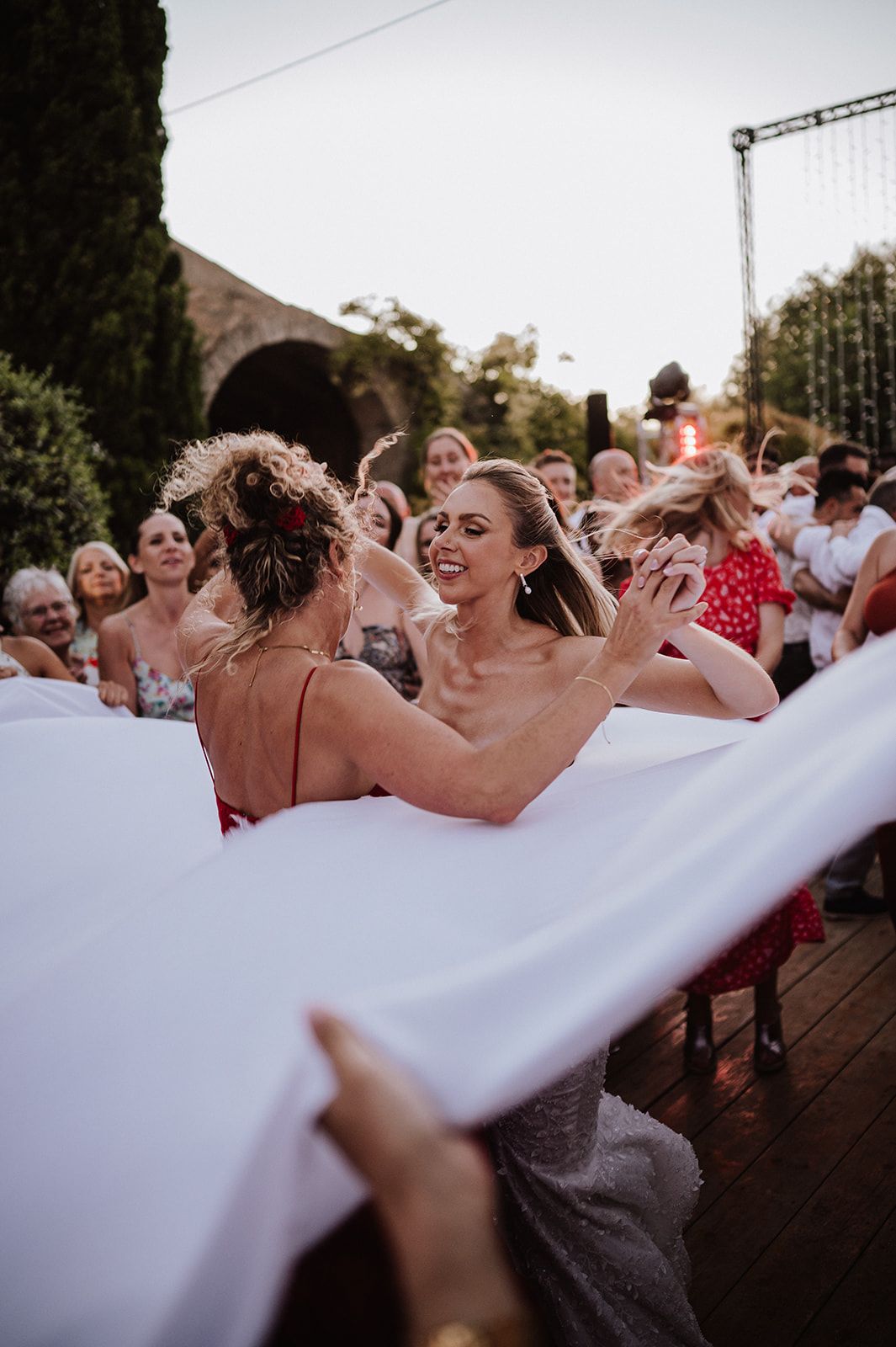Bride laughs joyfully with guest during lively outdoor wedding celebration at sunset.