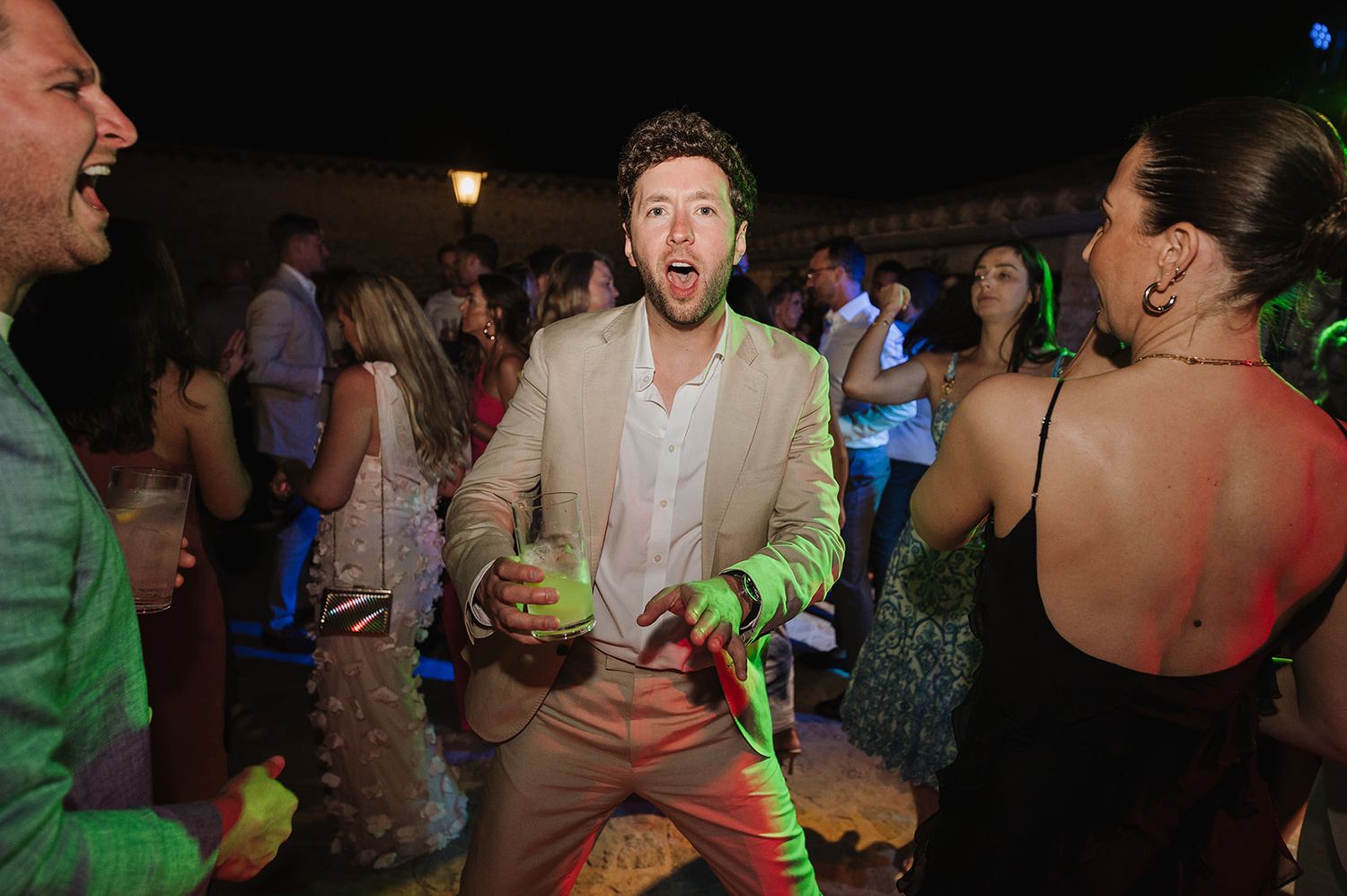 Man in beige suit dancing joyfully at an outdoor wedding reception party at night.