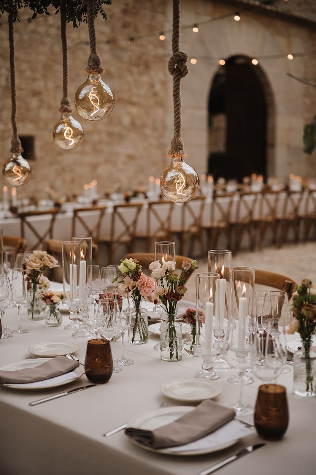 Elegant wedding reception table set with pink florals, candles, and vintage Edison bulb pendants.