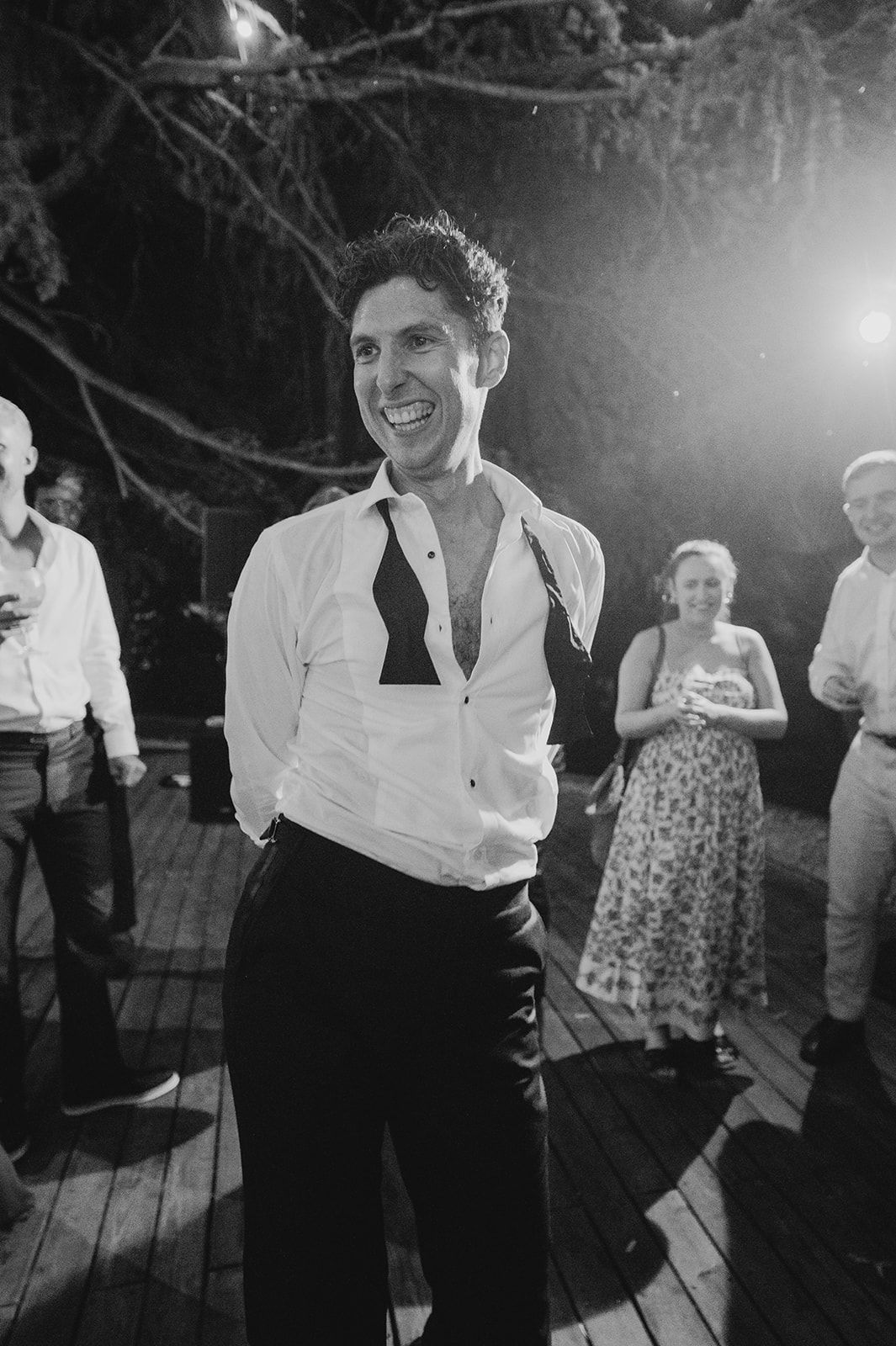 Man in white shirt dancing joyfully at an outdoor wedding reception at night.