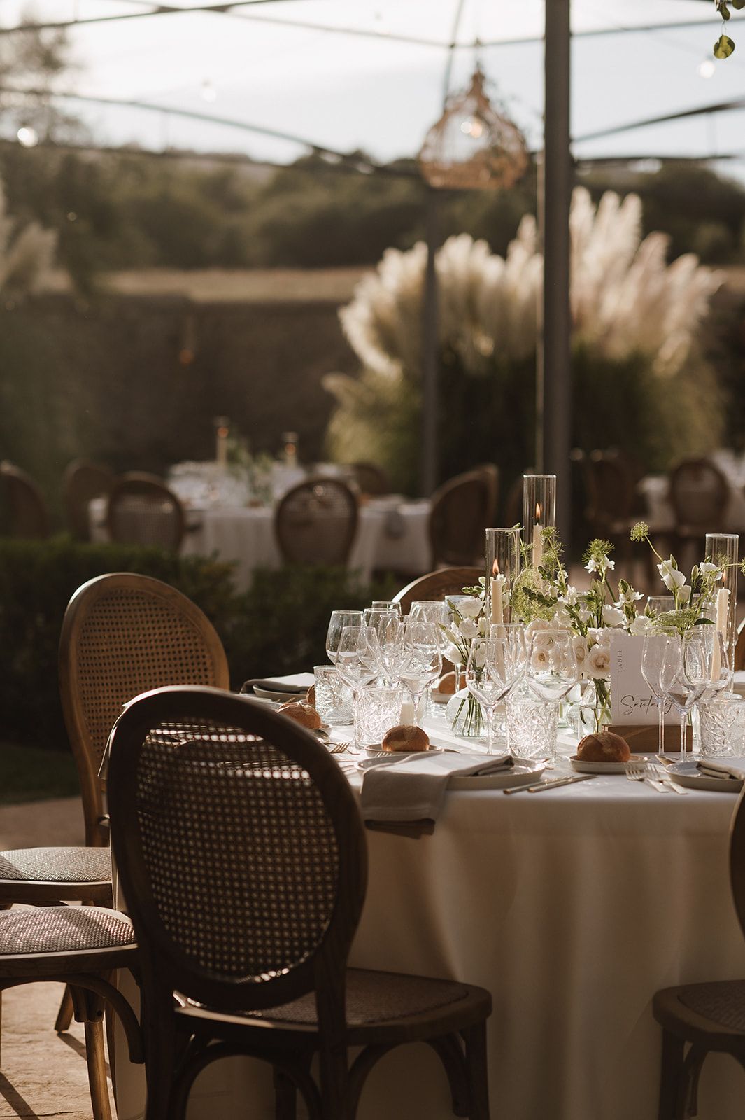 Elegant outdoor wedding reception table set with crystal glassware, candles, and delicate floral centerpieces.