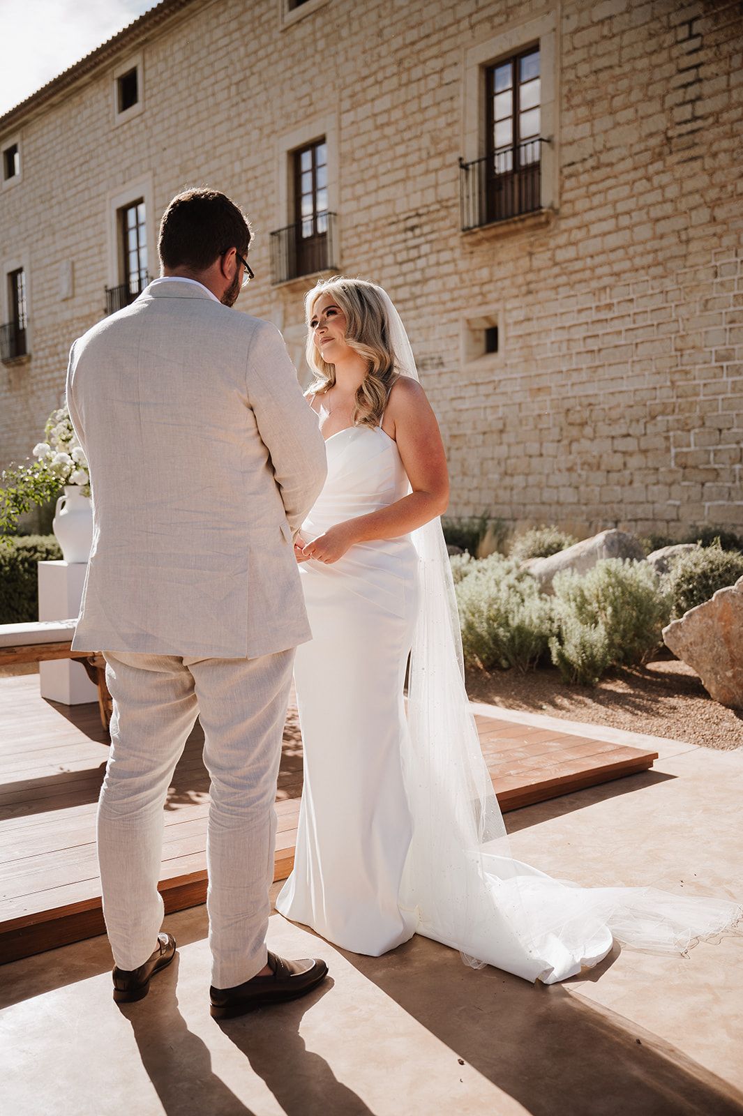 Bride and groom share a tender first look moment outside a rustic stone building on their wedding day.