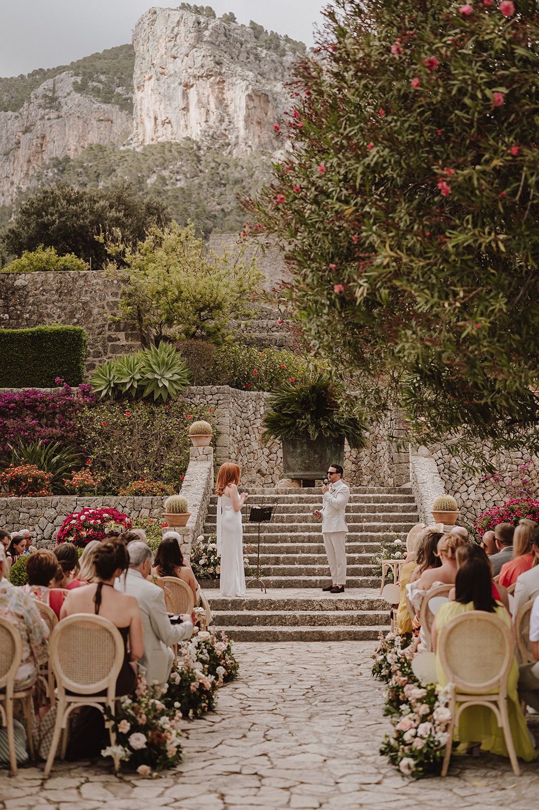 Elegant outdoor wedding ceremony on cobblestone aisle flanked by floral arrangements and rocky mountain views.