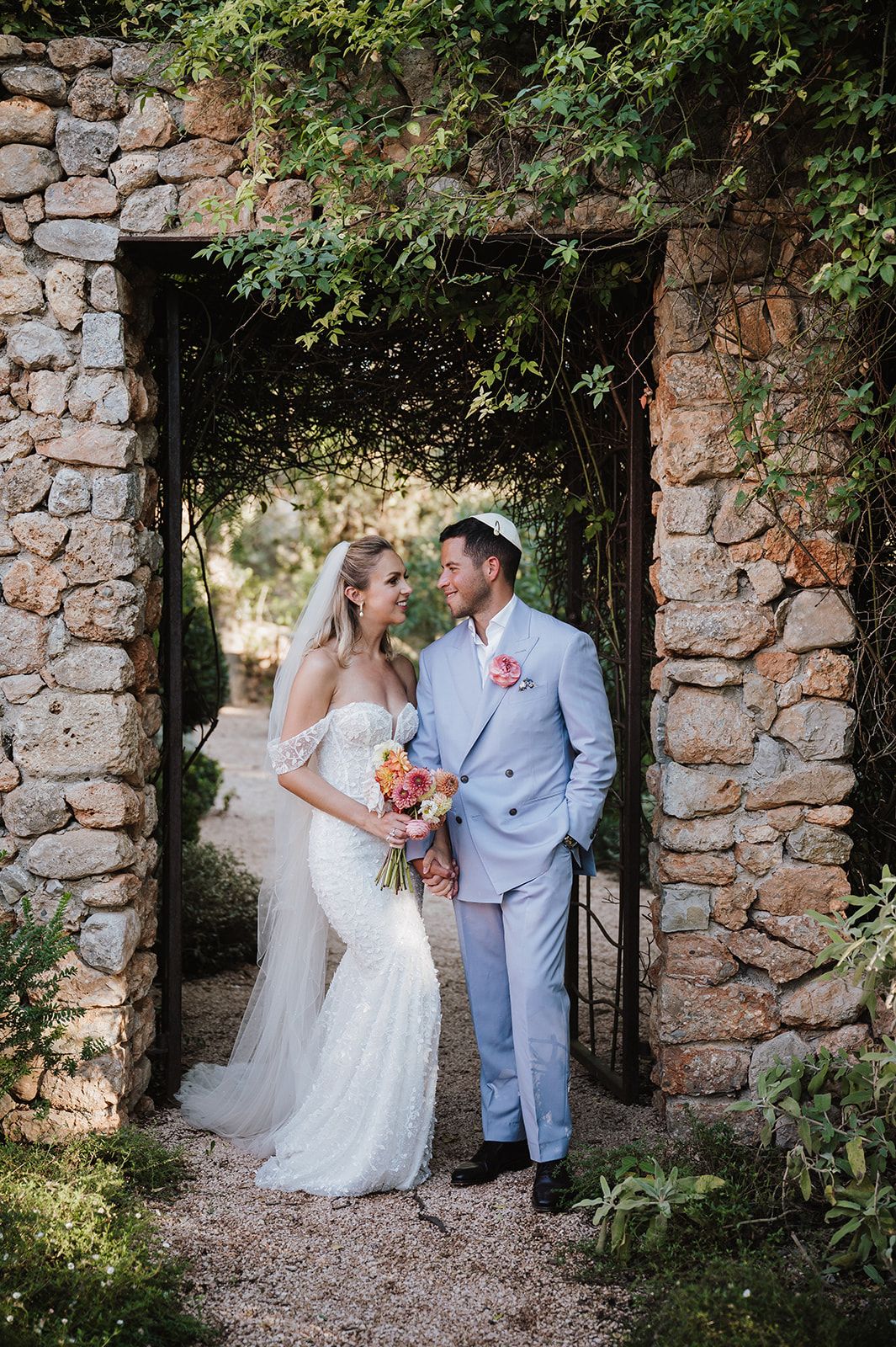Bride and groom share a romantic moment in a rustic stone archway covered with lush green vines.