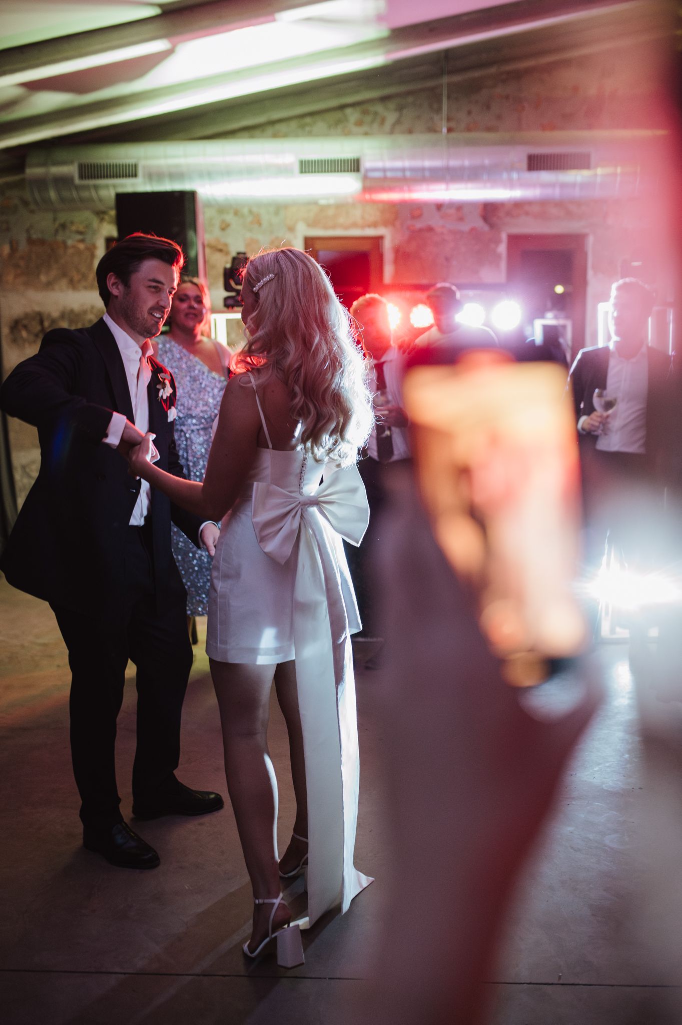Bride in white mini dress with bow dances with groom in suit at elegant wedding reception party.