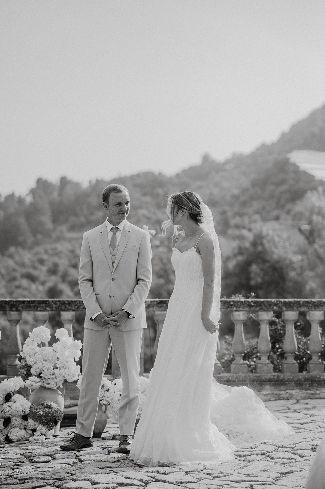 Black and white photo of smiling groom and emotional bride during outdoor wedding ceremony on stone terrace.