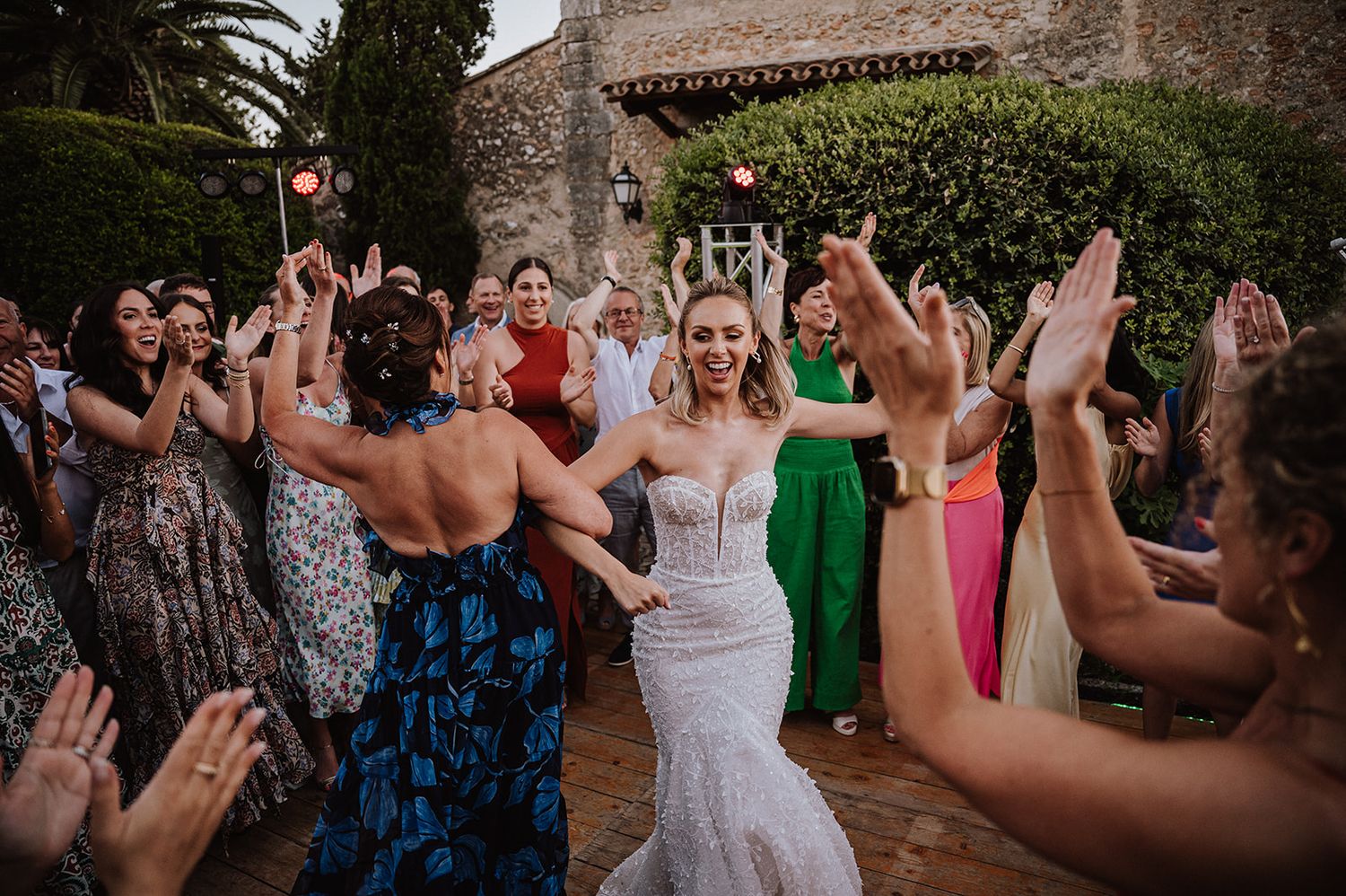 Bride in beaded mermaid gown celebrates with cheering guests at a festive outdoor wedding reception.
