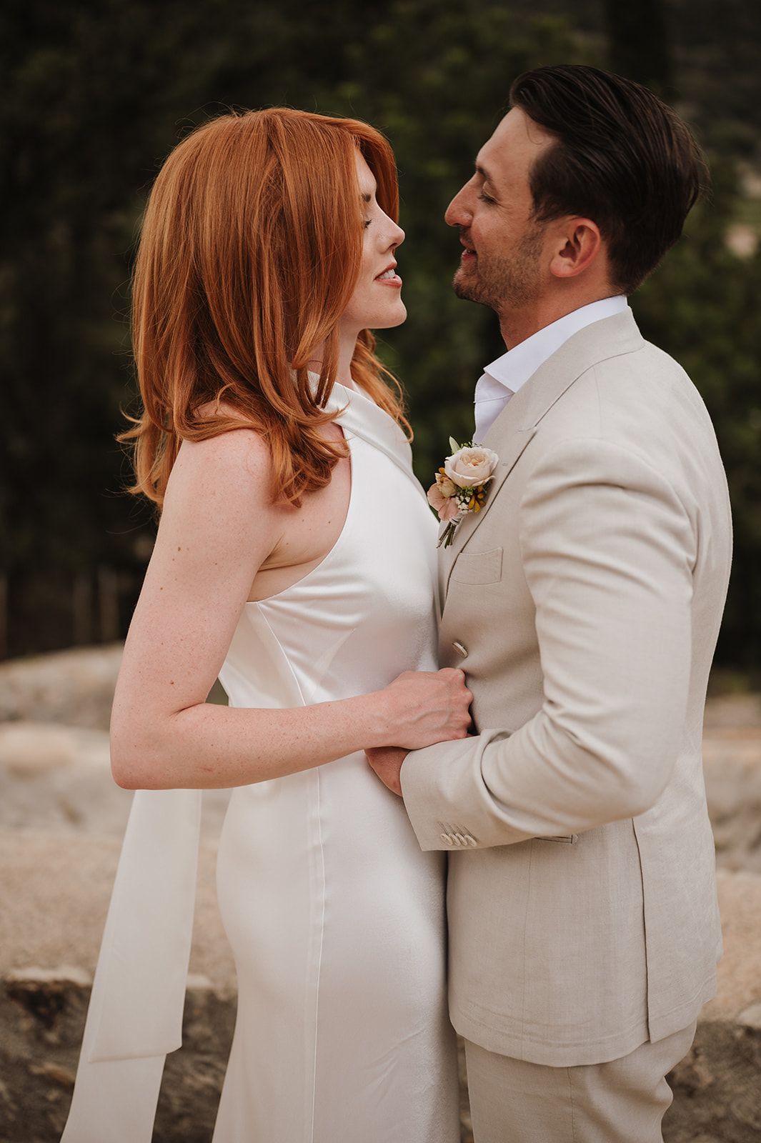 Bride in white halter gown and groom in beige suit share a joyful moment at their outdoor wedding.