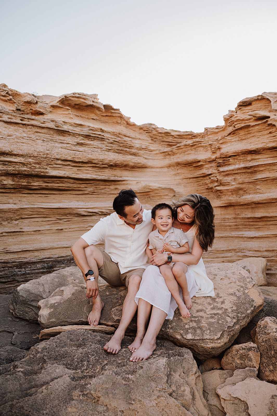 Happy family of three sitting on rocks in a scenic sandstone canyon at sunset.