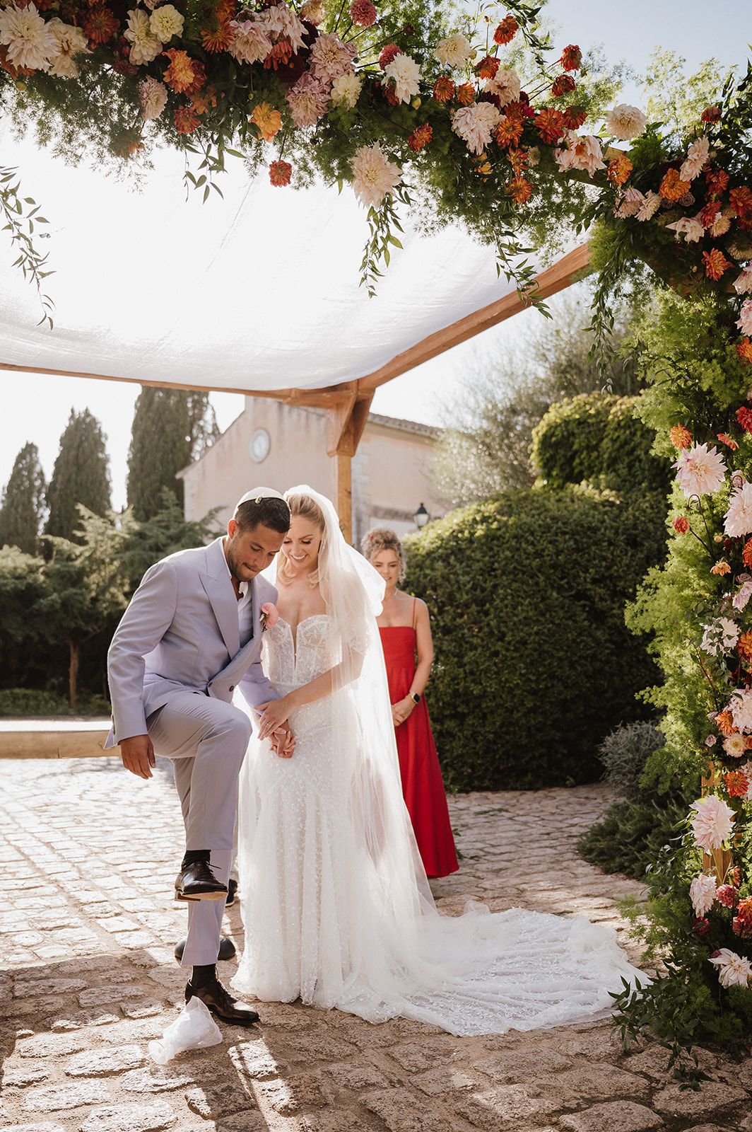 Bride and groom share a tender moment under a floral arch during an outdoor wedding ceremony.